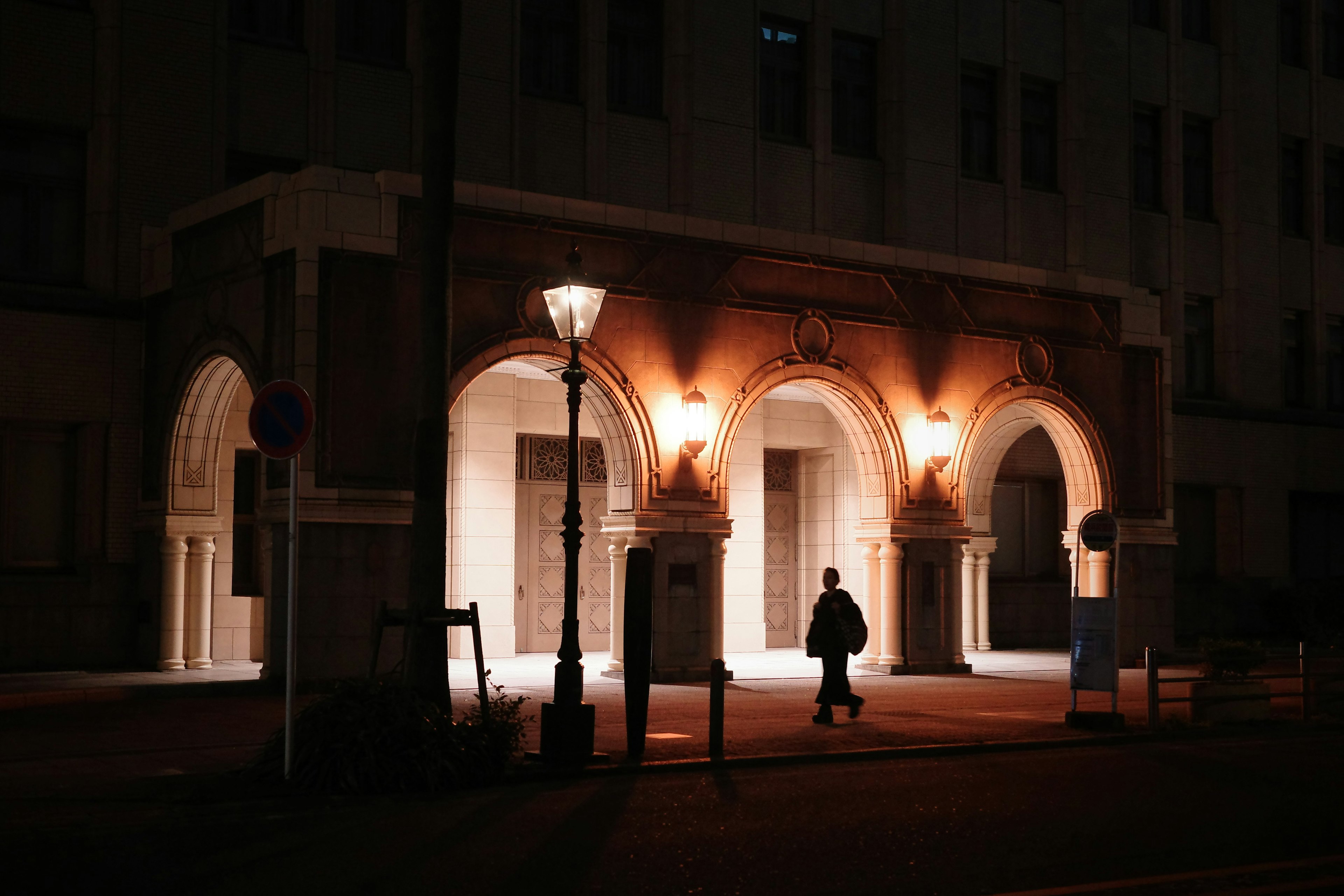 Una persona de pie bajo farolas cerca de un edificio con arcos por la noche