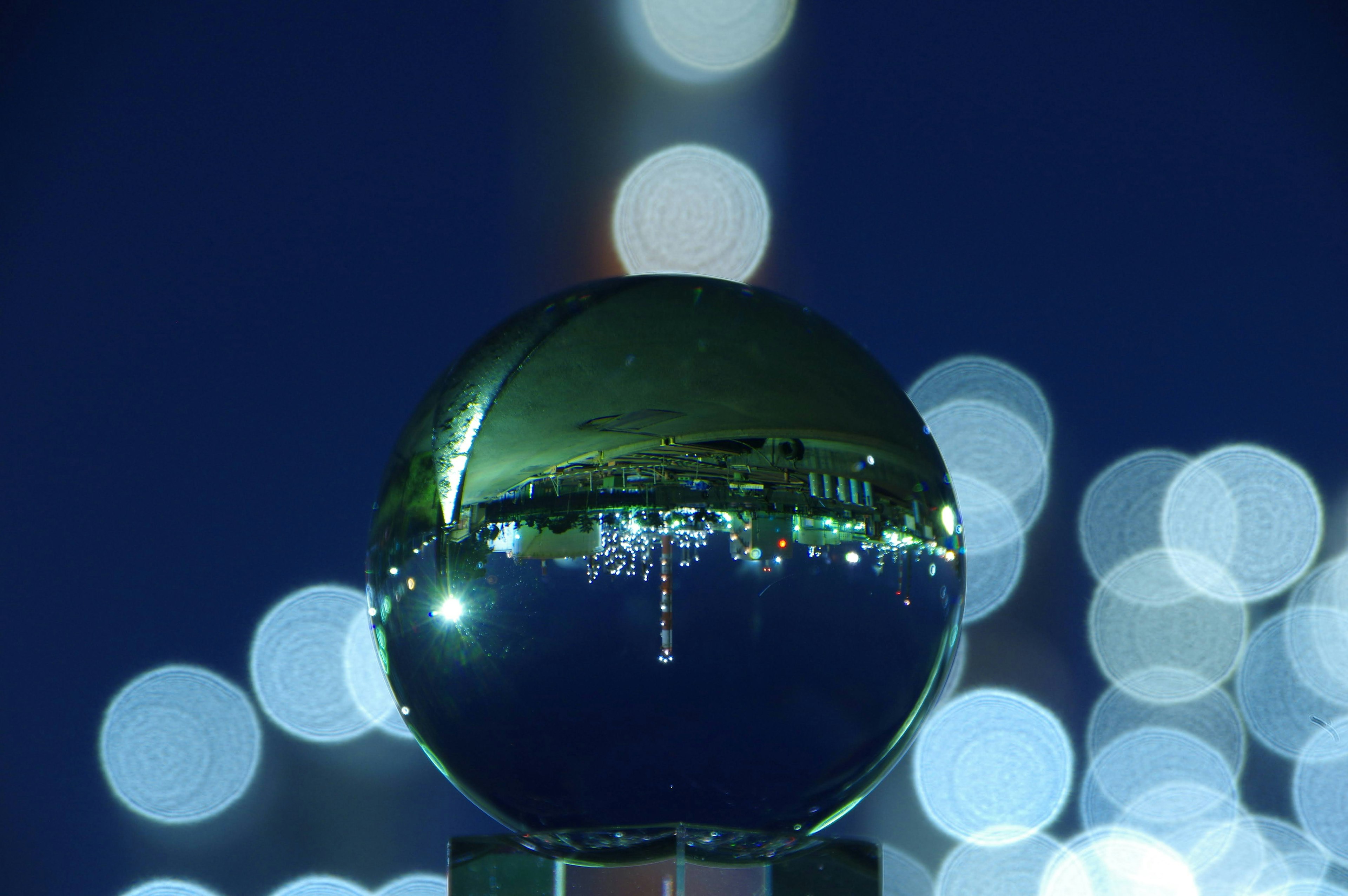 Esfera de vidrio reflectante que muestra un paisaje urbano con luces desenfocadas