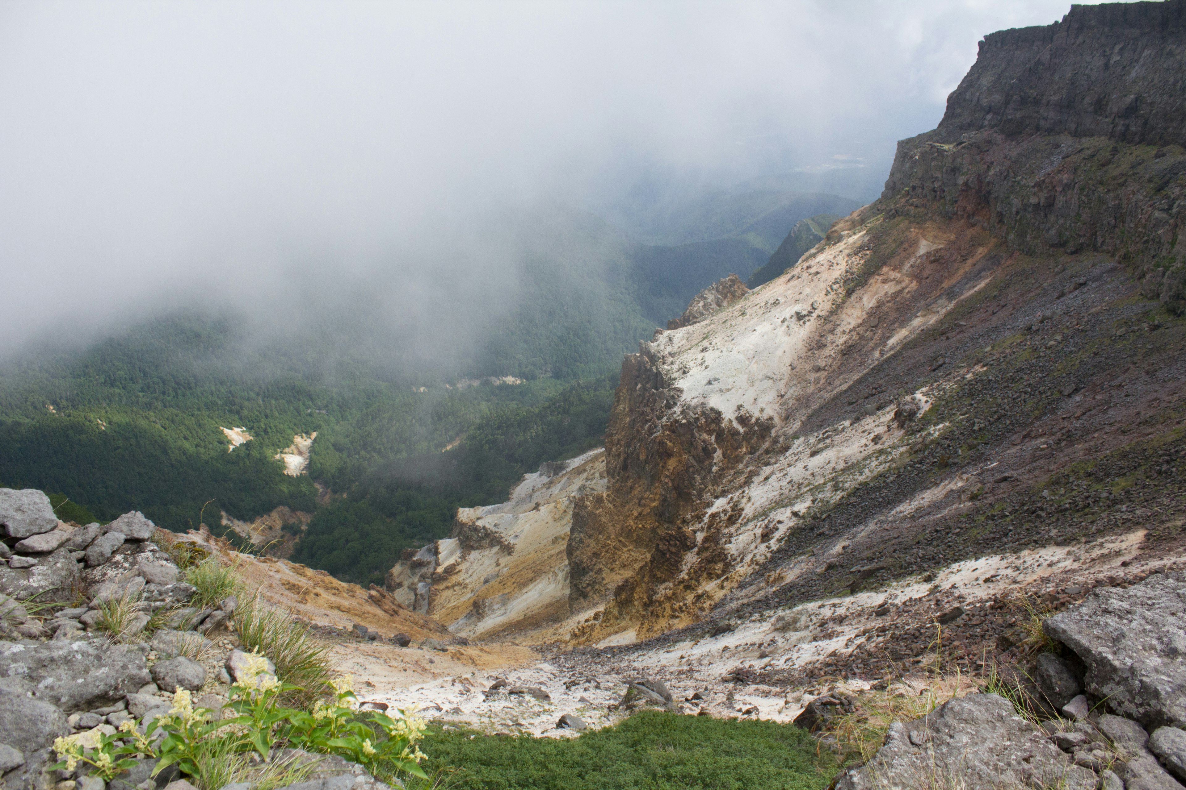 Steiler Berghang mit einem von Wolken bedeckten Tal