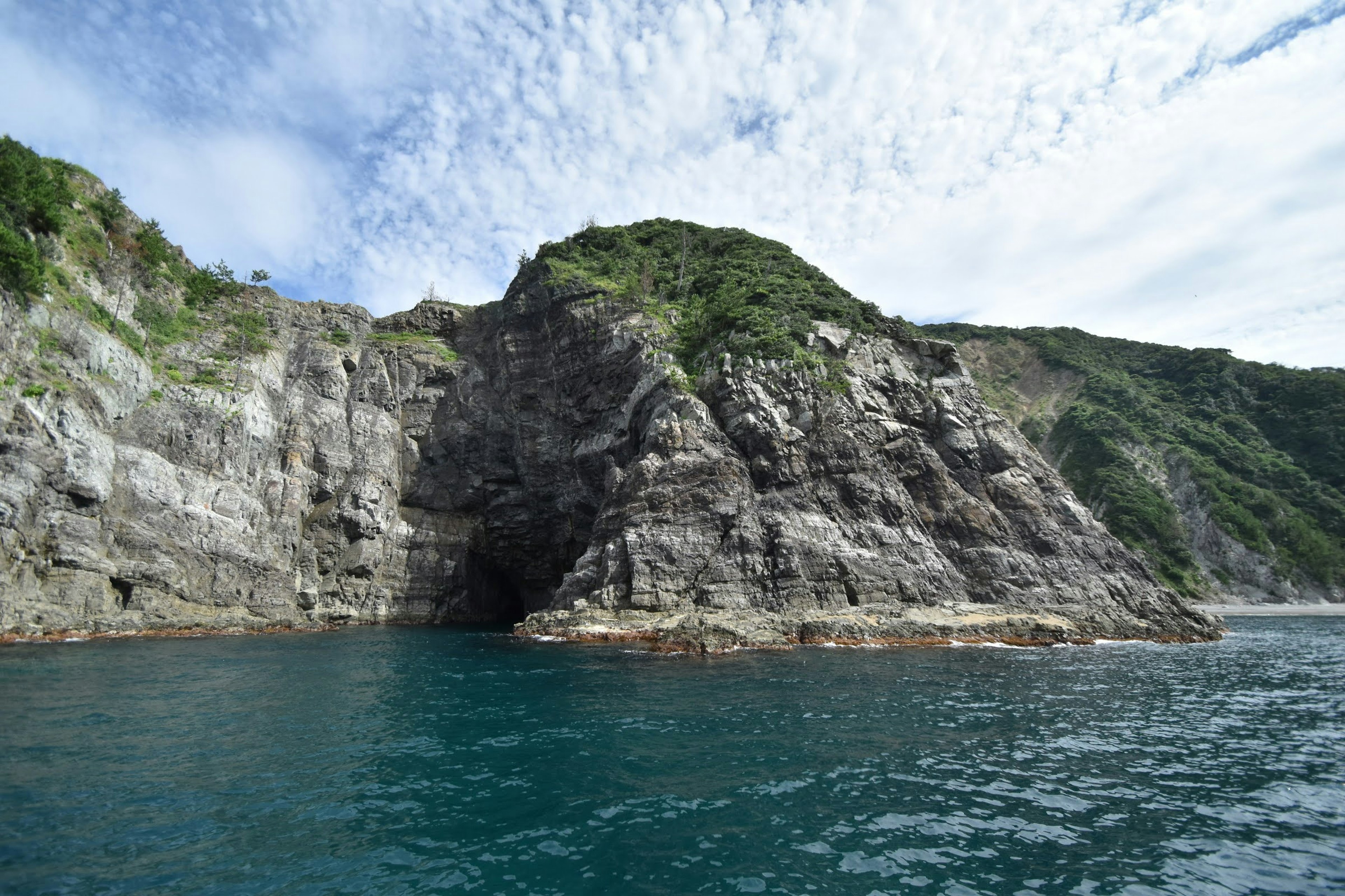 海岸岩石和绿色山丘在多云的天空下