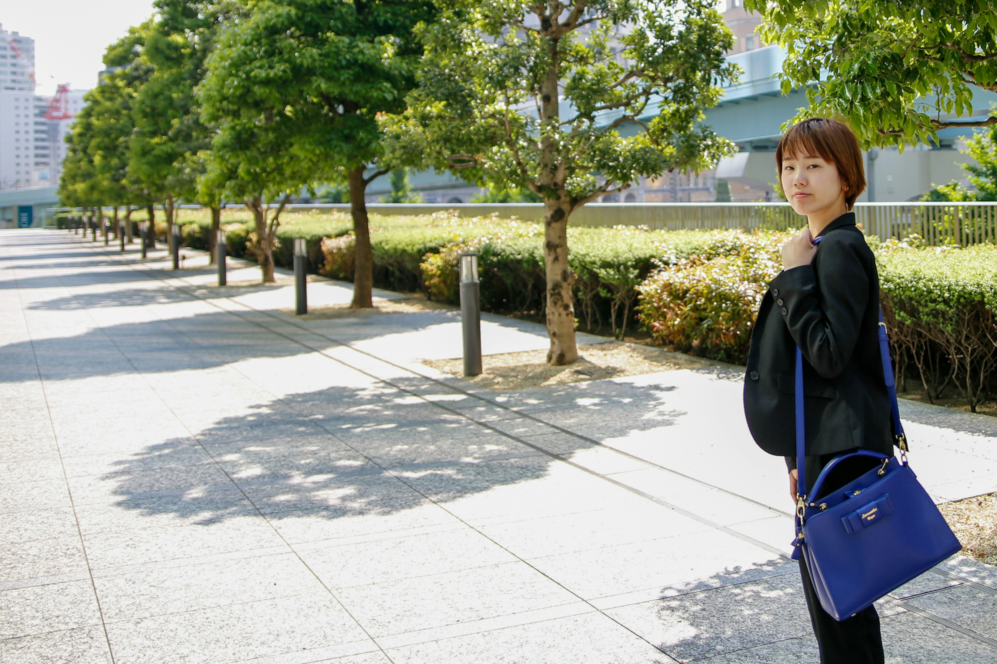 青いバッグを持った女性が公園の道を歩いている