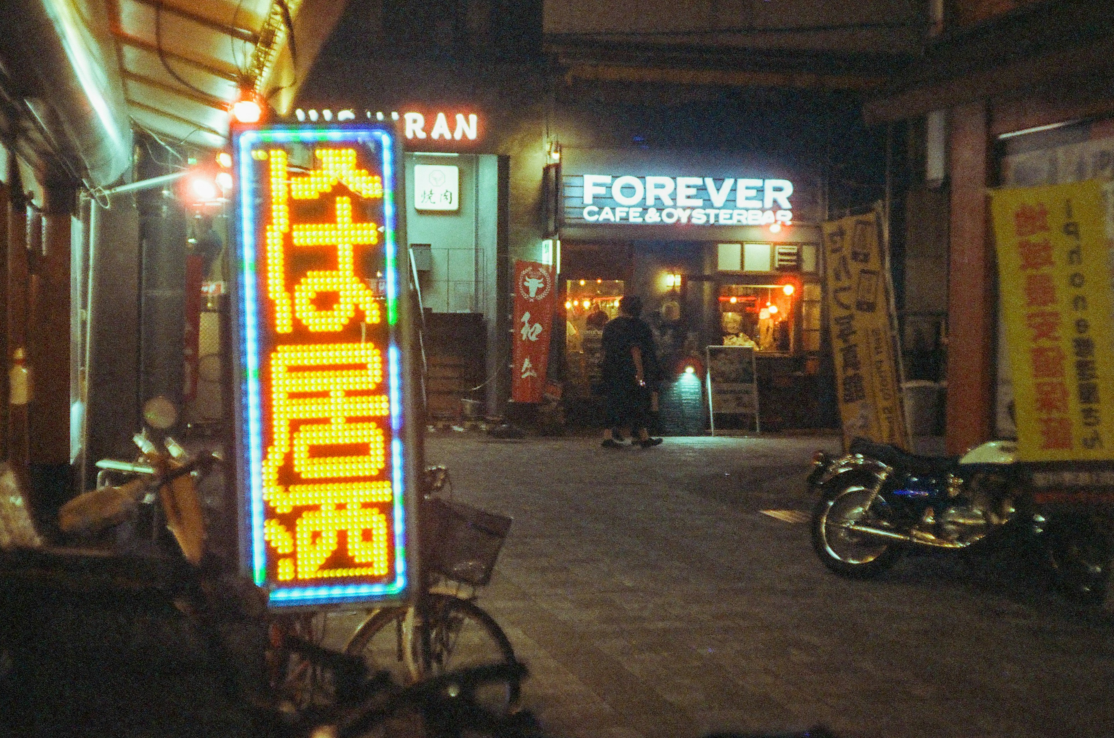 ฉากถนนกลางคืนที่มีป้ายไฟนีออนและร้านอาหาร