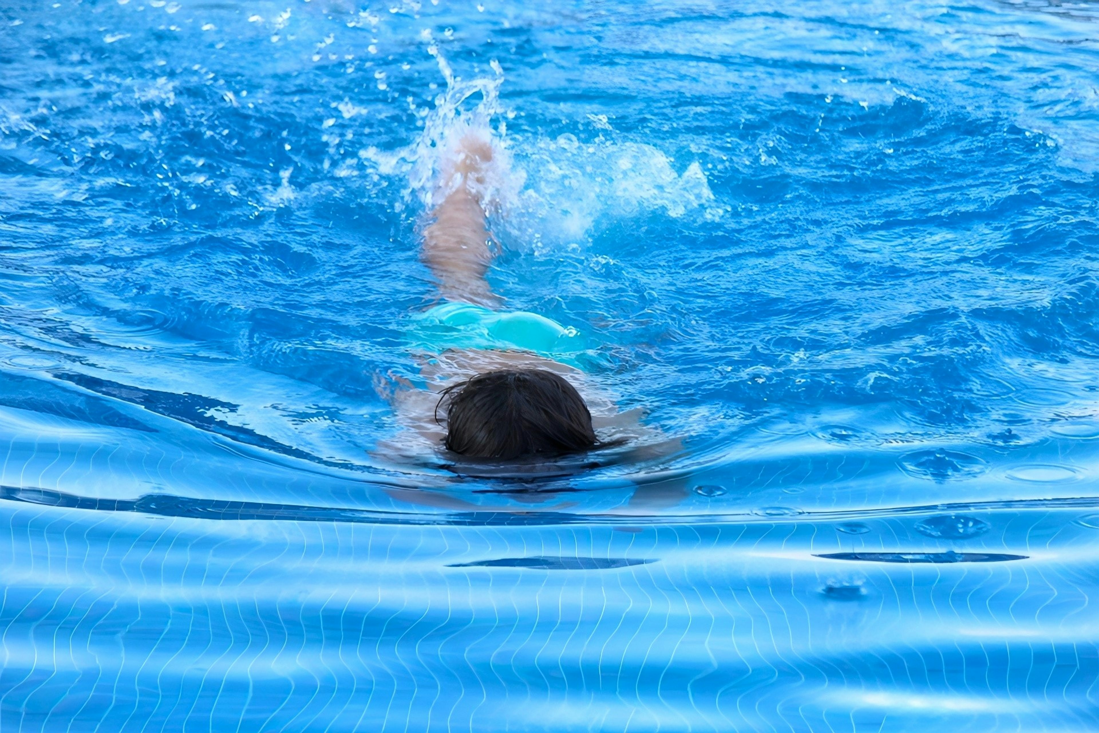 Enfant nageant dans une piscine, eau bleue avec des ondulations