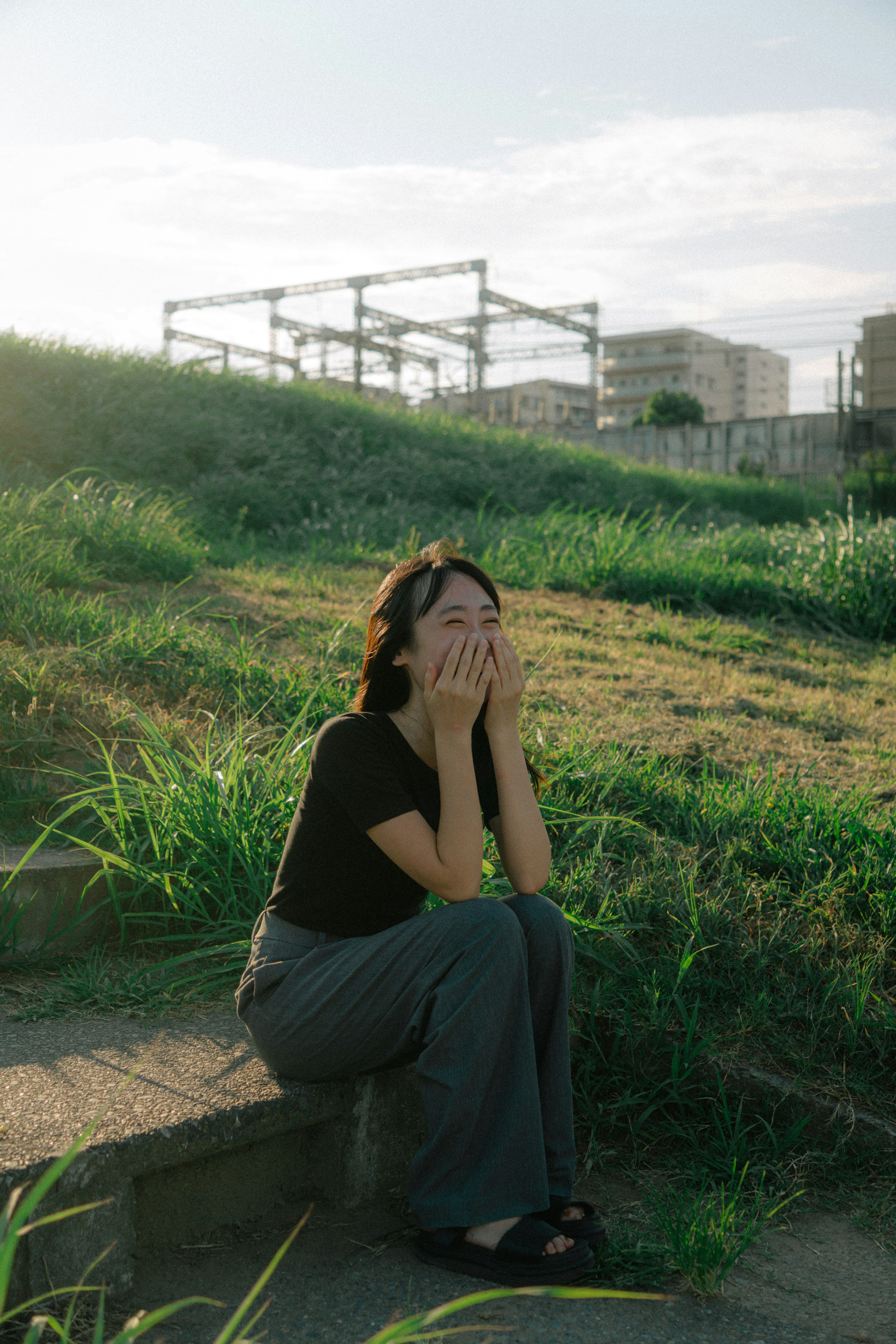 A young woman sitting in grass with her hands covering her face