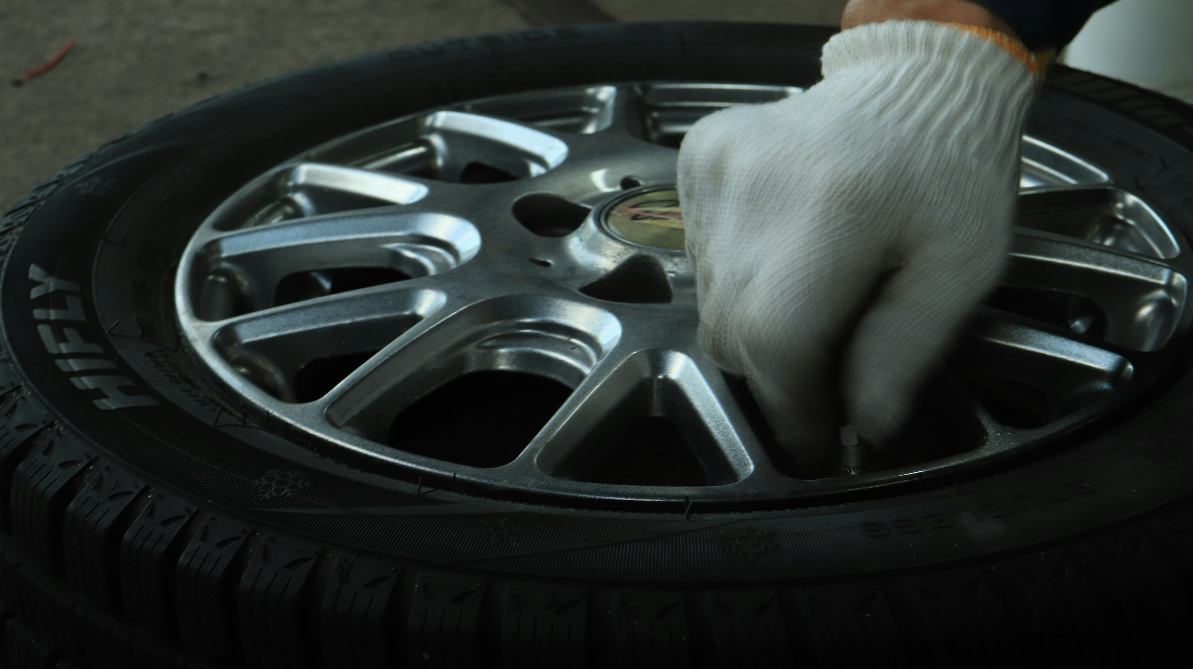 Mano guantata che lavora su una ruota d'auto con pneumatico