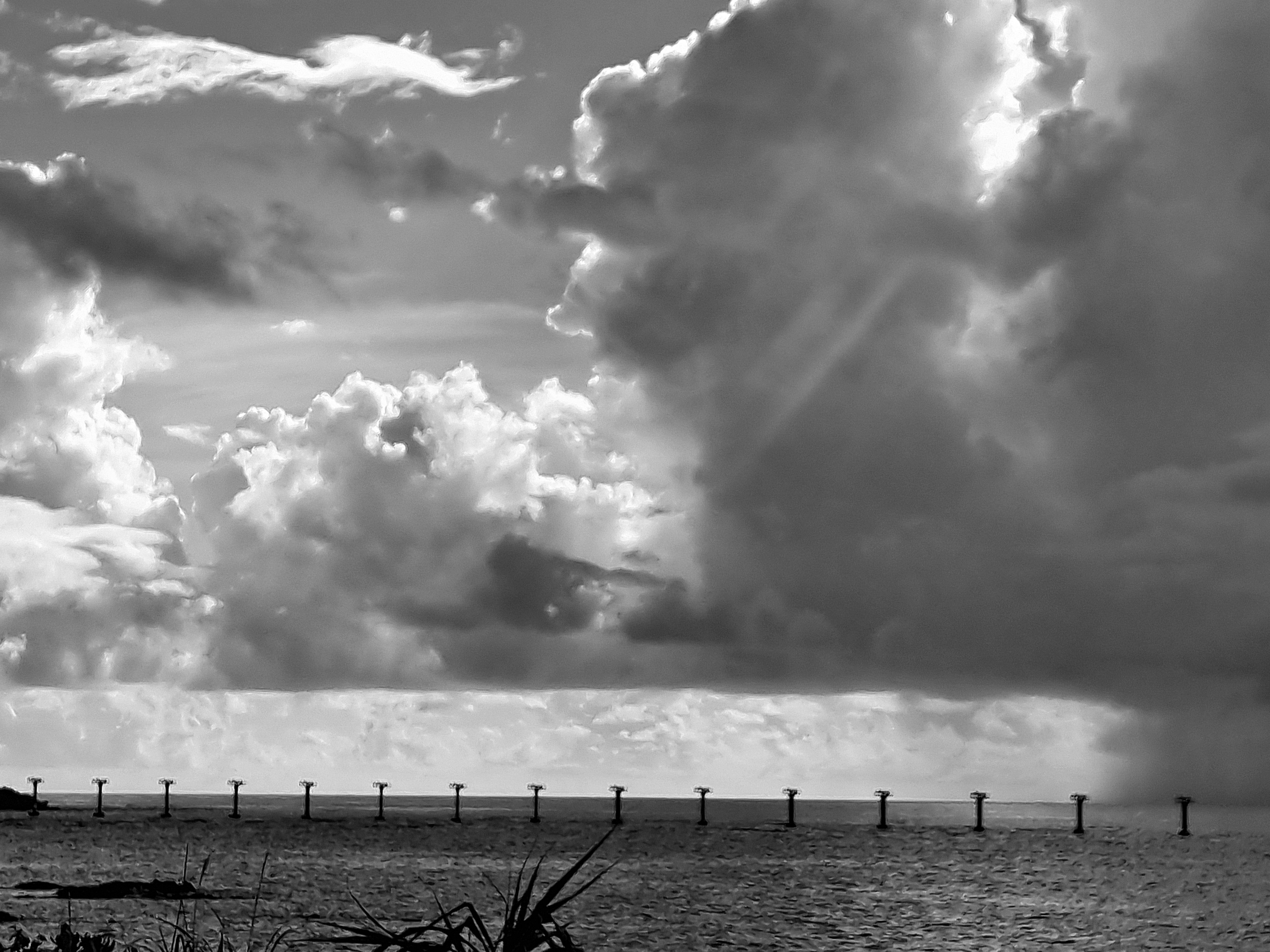 Schwarzweißbild einer Brücke über dem Meer mit dramatischen Wolken