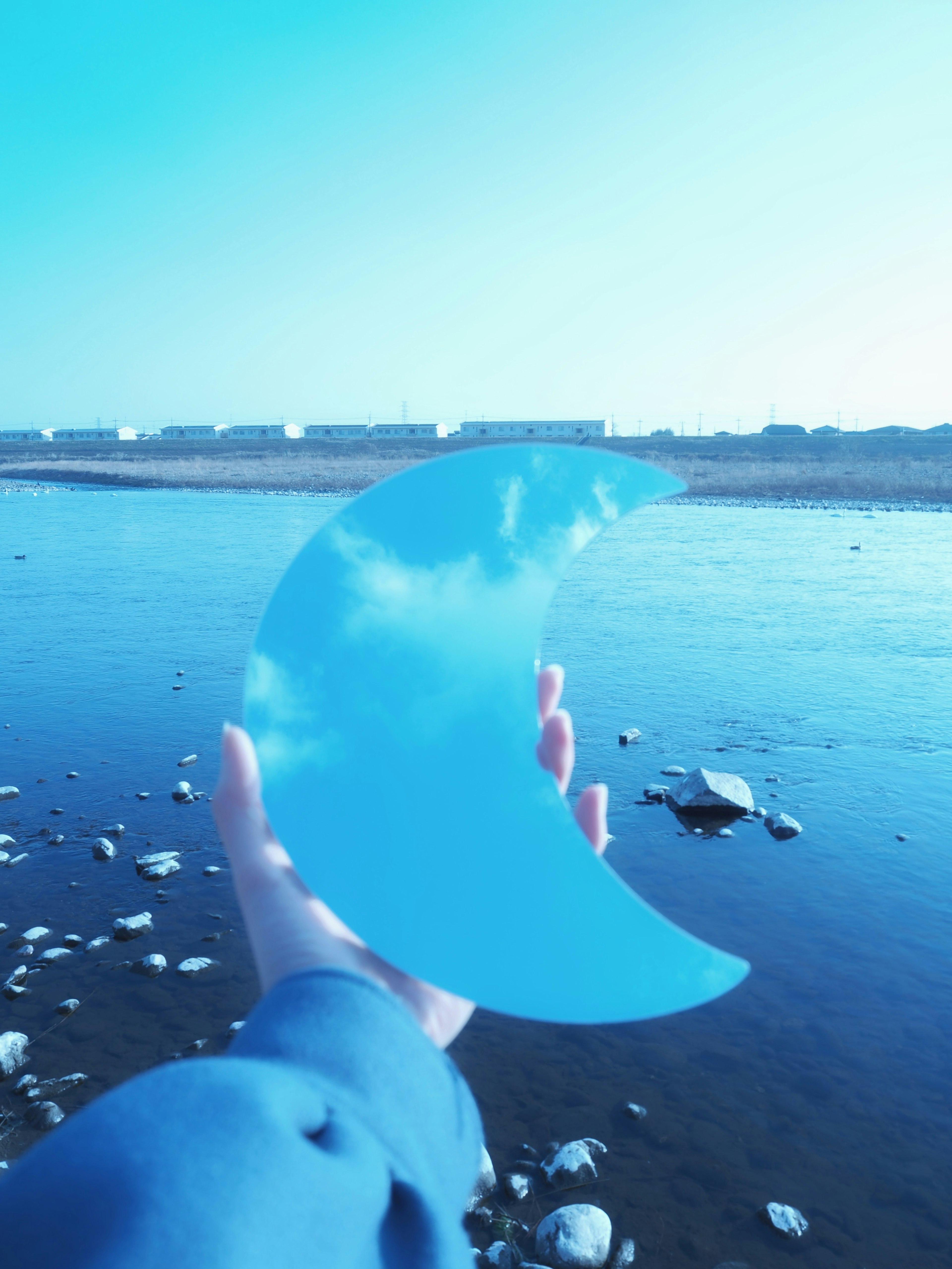 Mano sosteniendo un objeto transparente en forma de media luna azul con un fondo de río