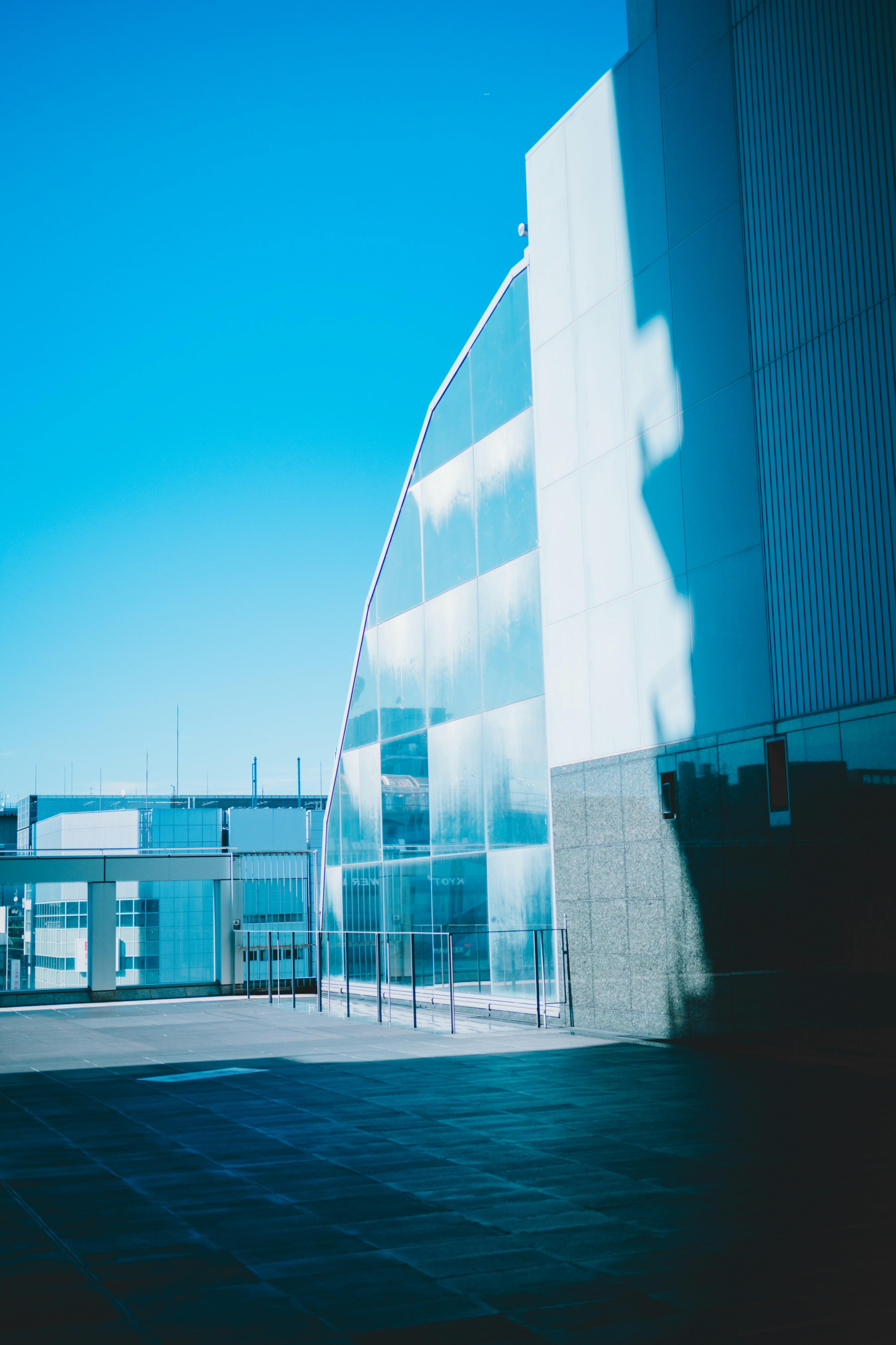 Modern building exterior under blue sky with glass reflections and striking shadows