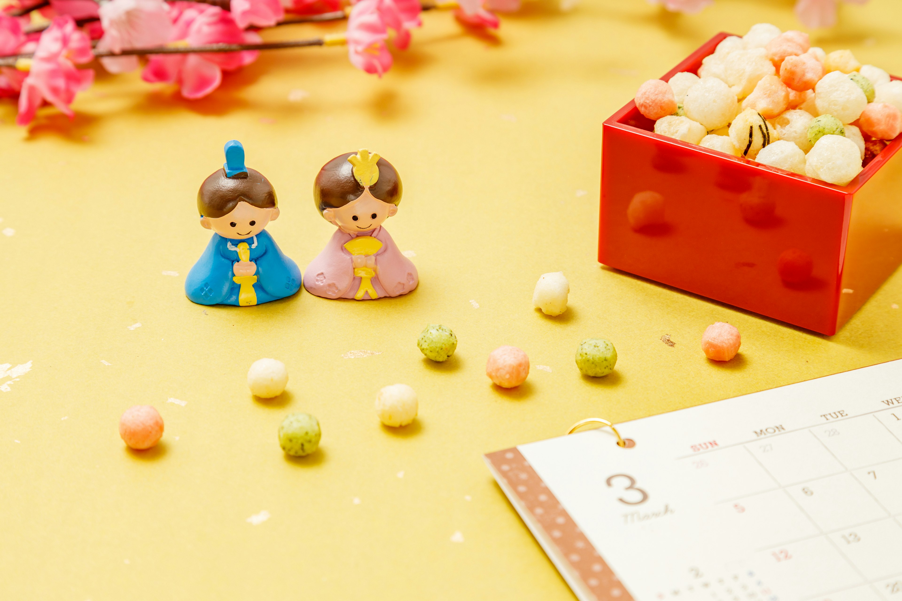 Hinamatsuri dolls on a yellow background with a box of sweets