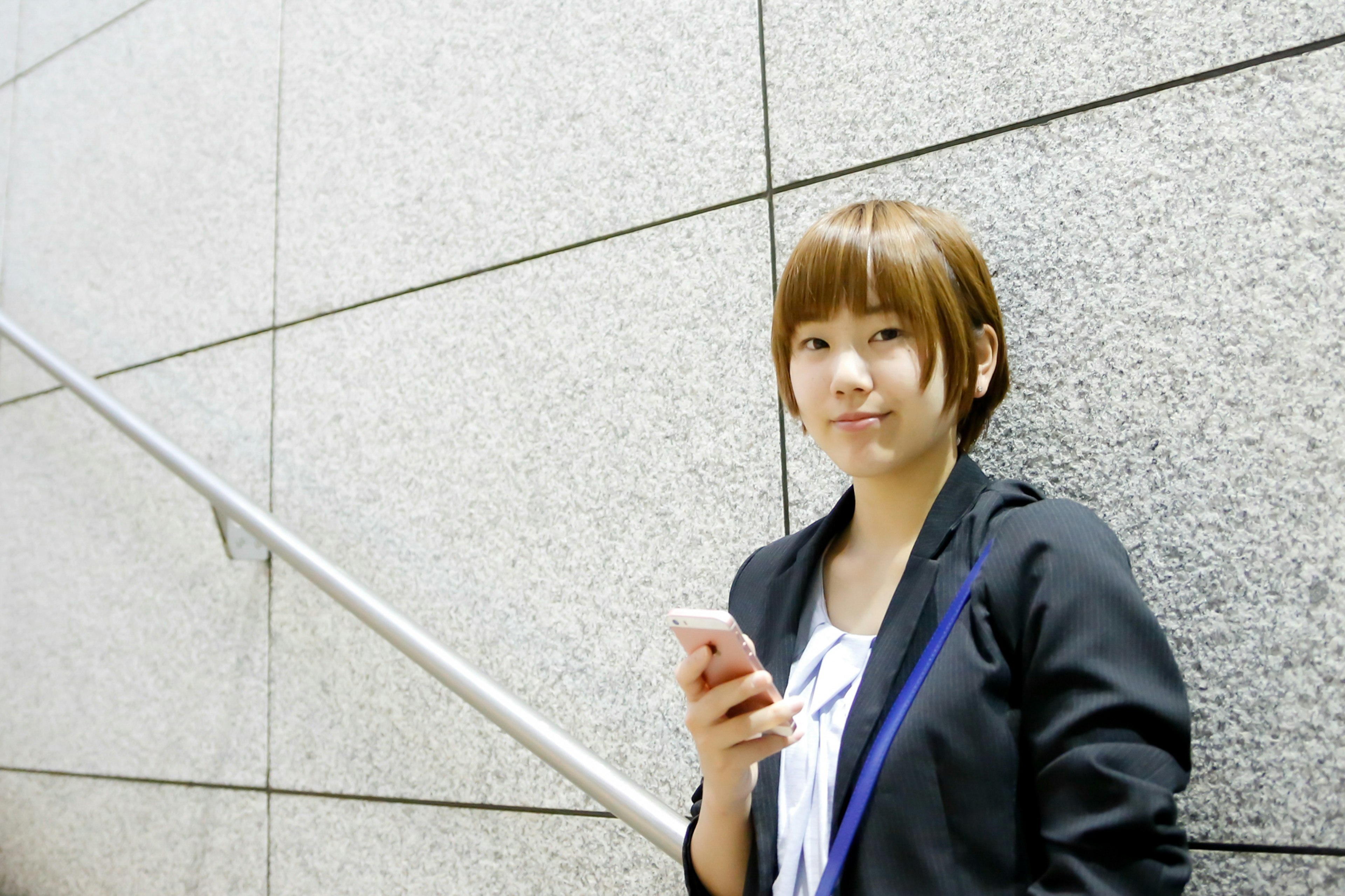 Young woman holding a smartphone leaning against a wall