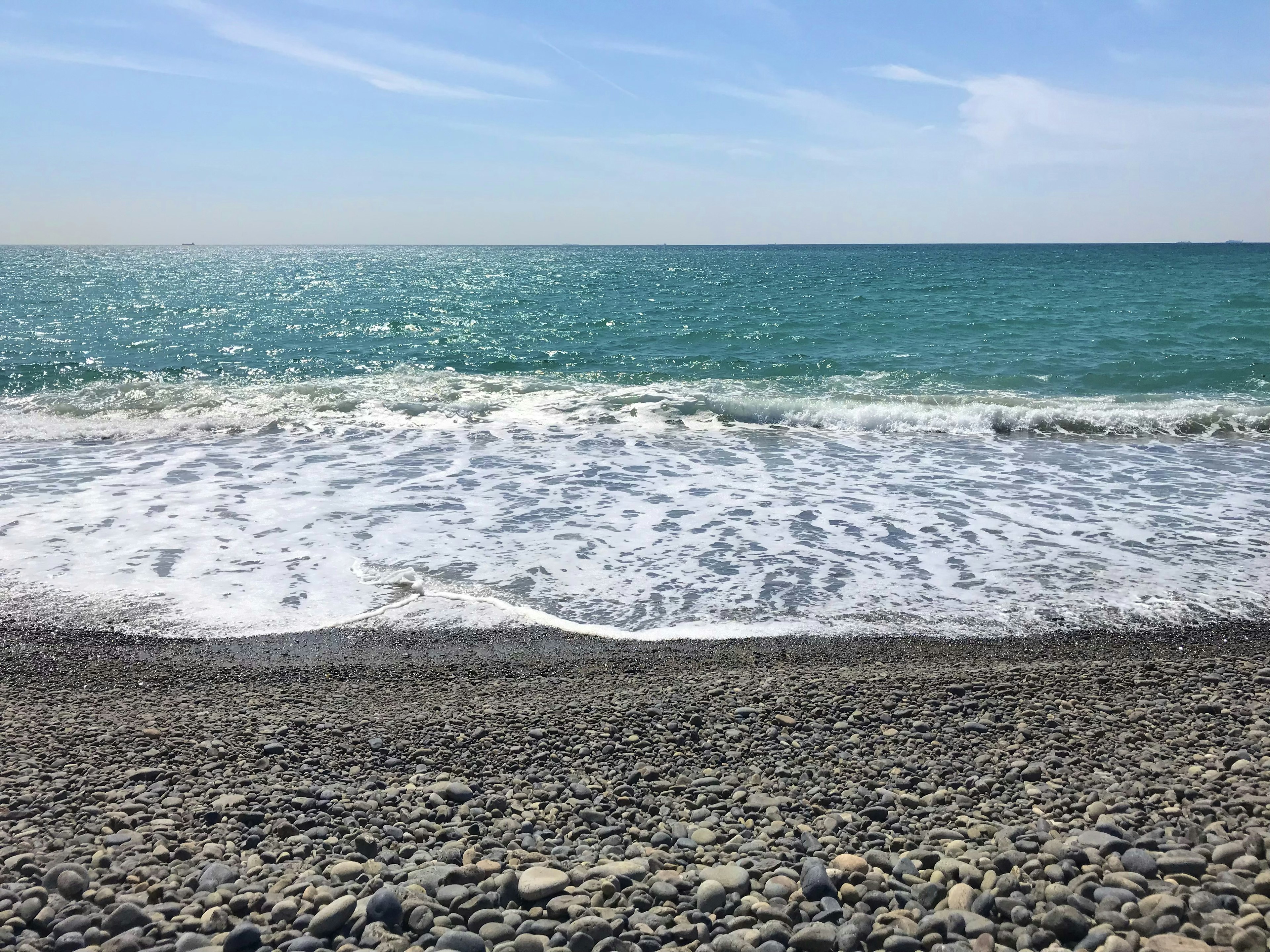 風景如畫的卵石海灘，碧綠色的水和柔和的波浪