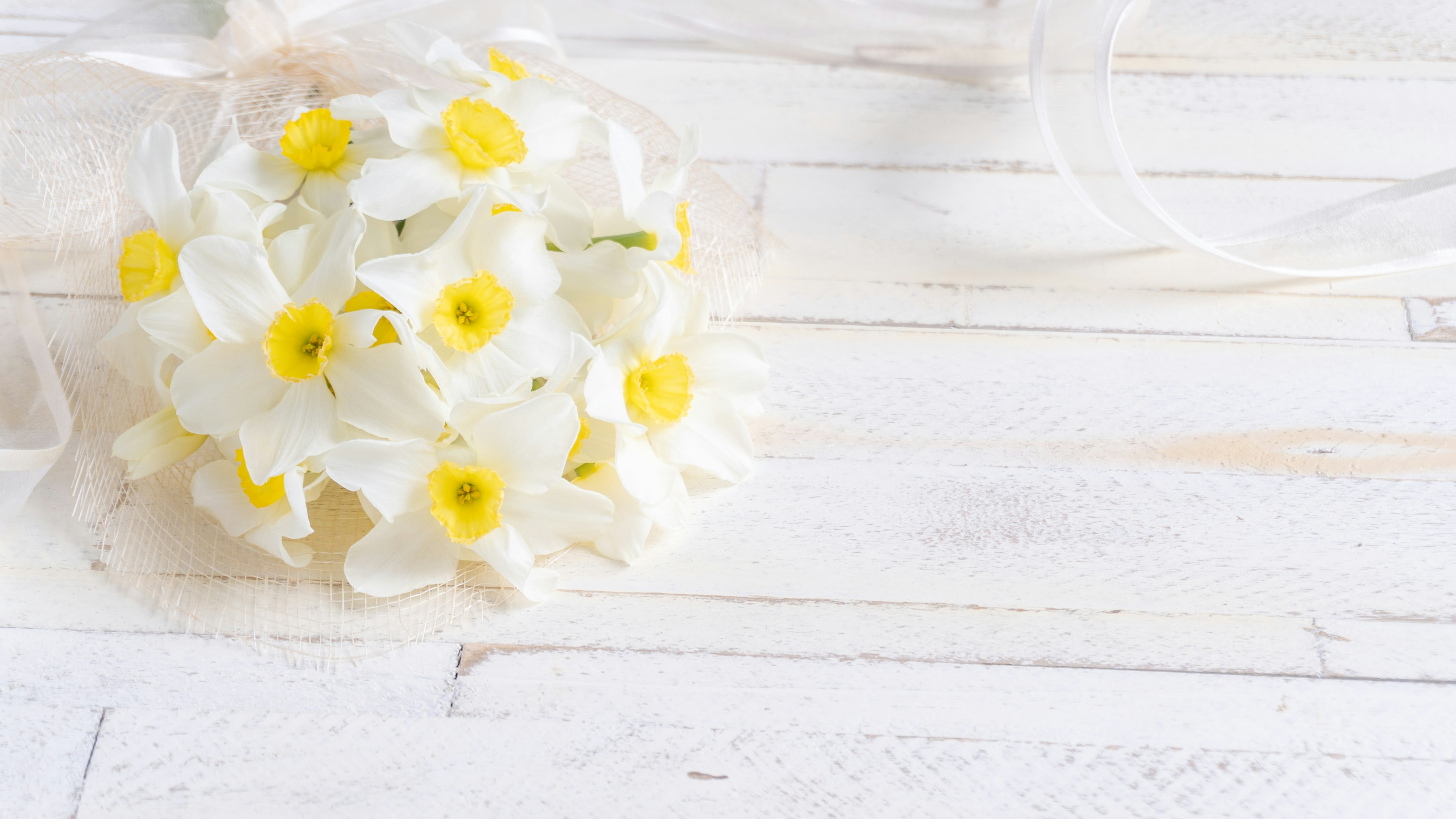 Un bouquet di fiori bianchi con centri gialli posato su un tavolo di legno bianco