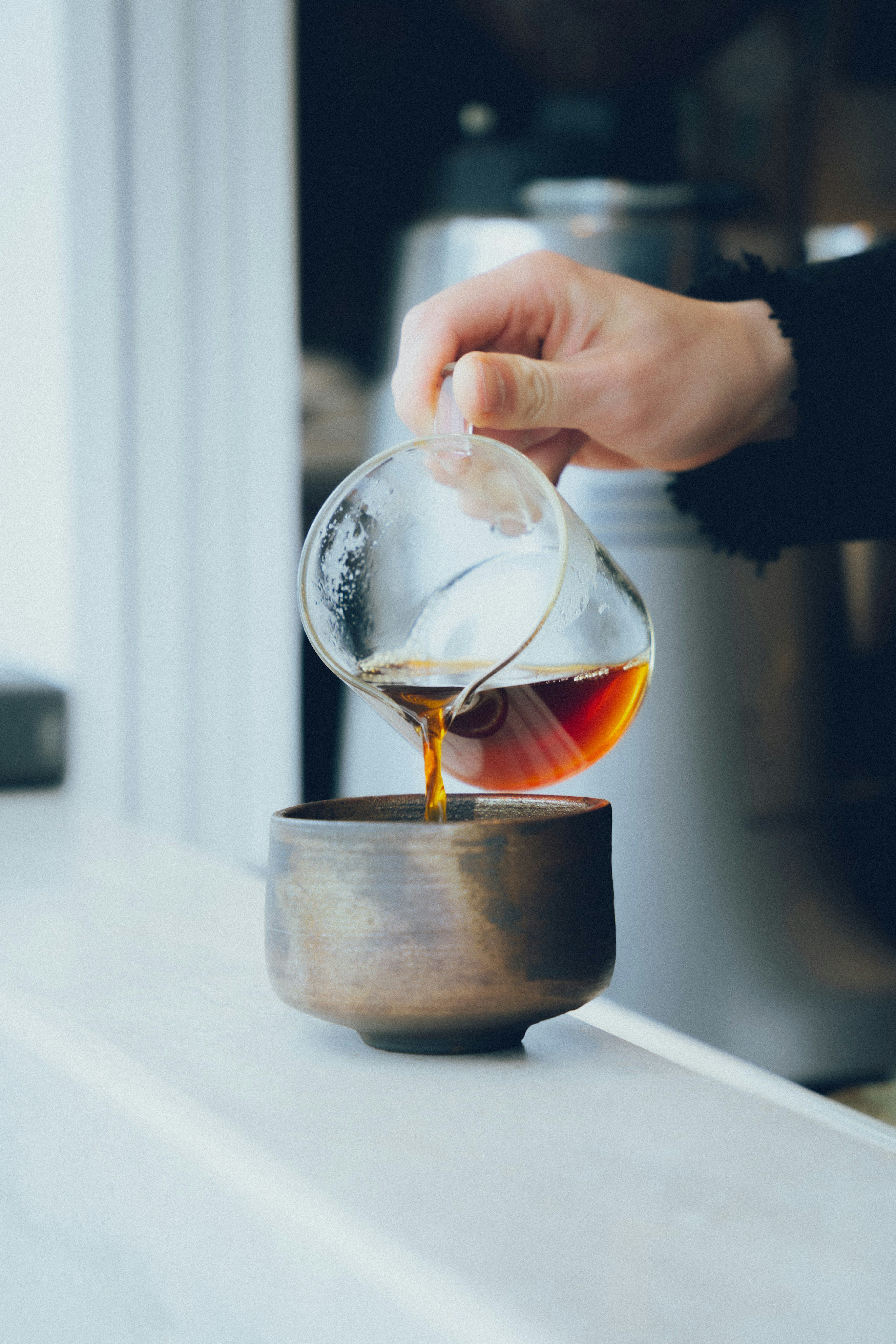 Una mano vertiendo café de un recipiente de vidrio en una taza de cerámica