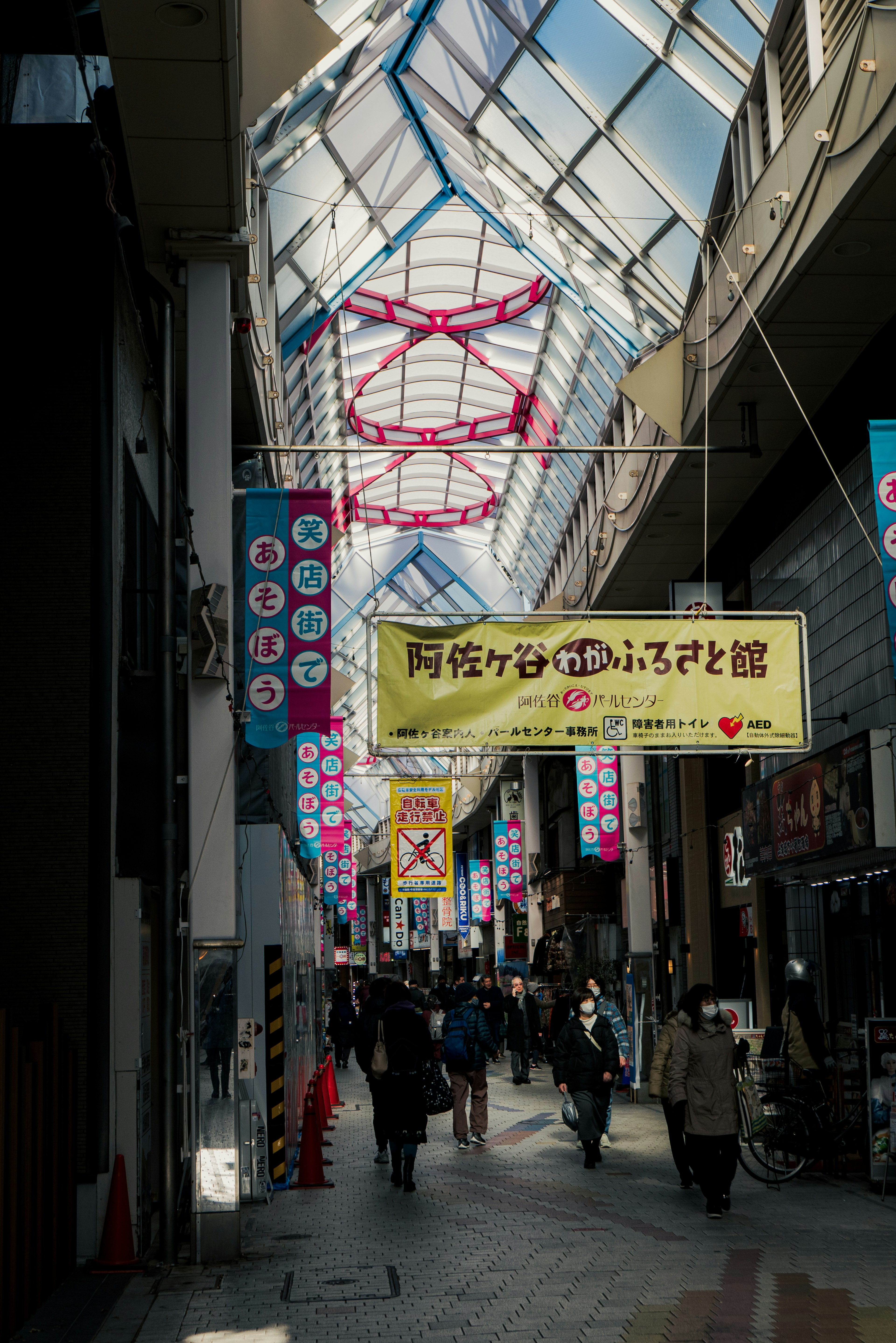 A bustling shopping street with a glass ceiling and colorful banners overhead