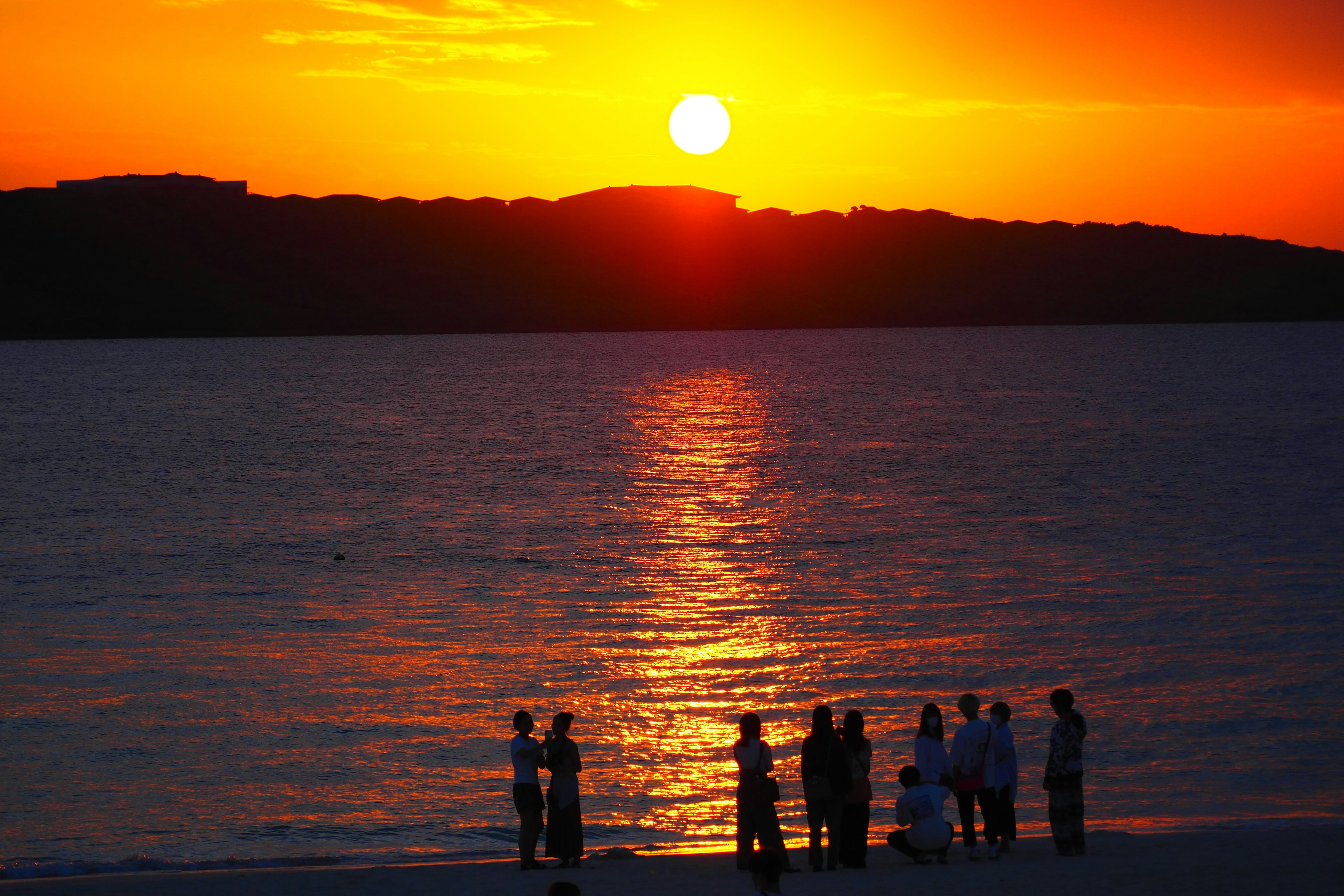 Orang-orang berkumpul di pantai saat matahari terbenam