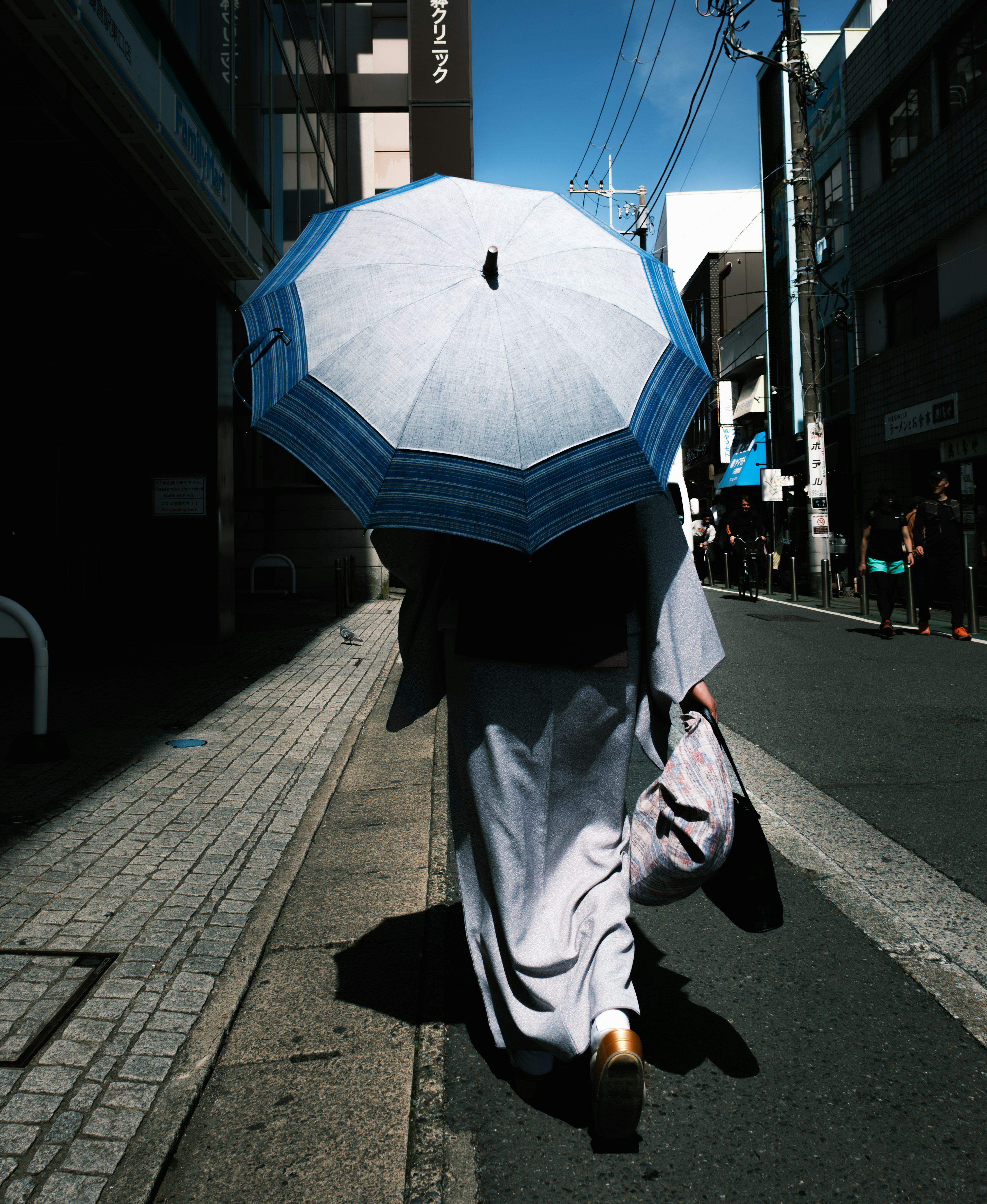 一位穿着和服的女性在街上走，手持白色雨伞