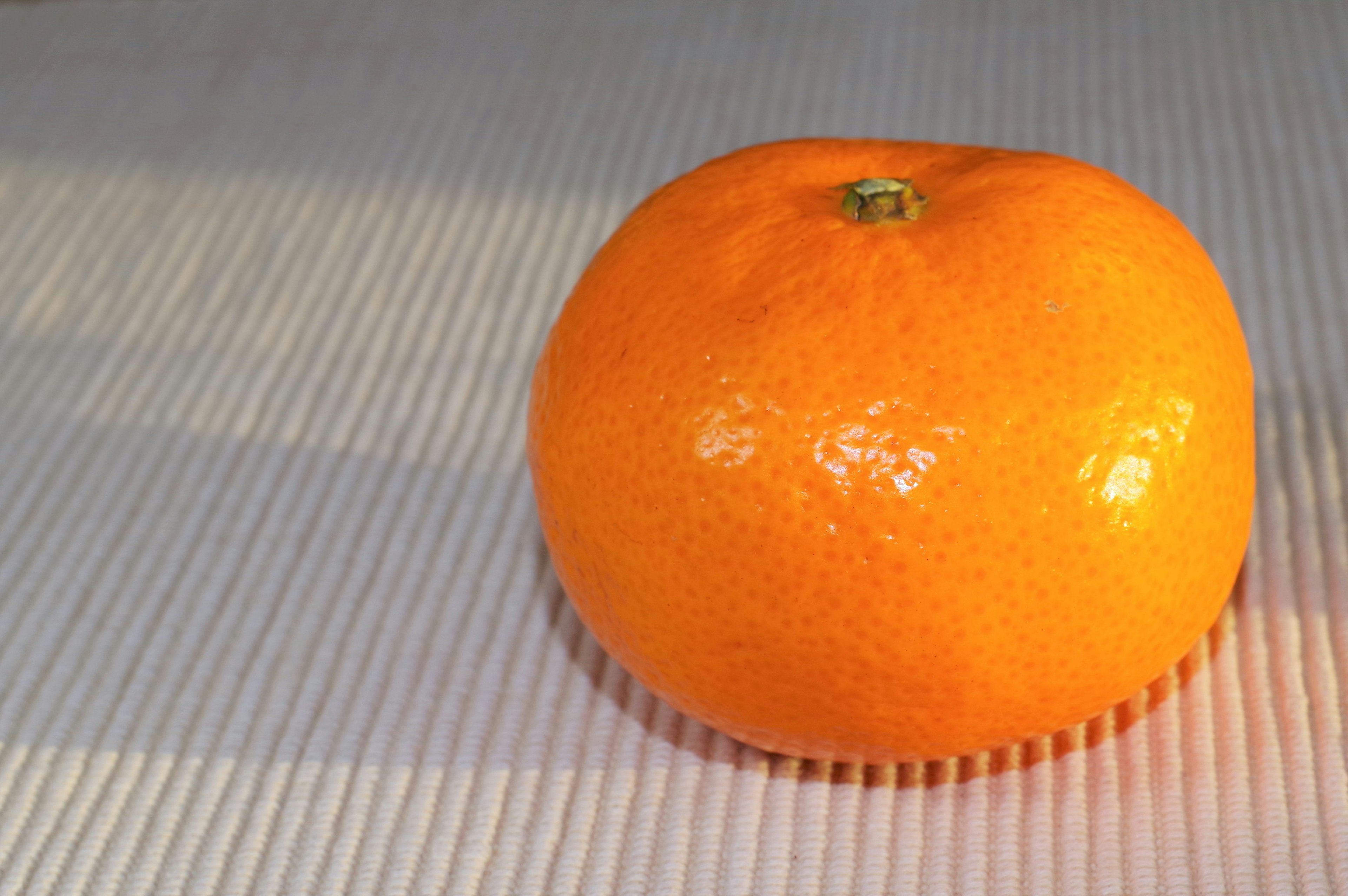 Un fruit orange vif reposant sur une surface à rayures blanches