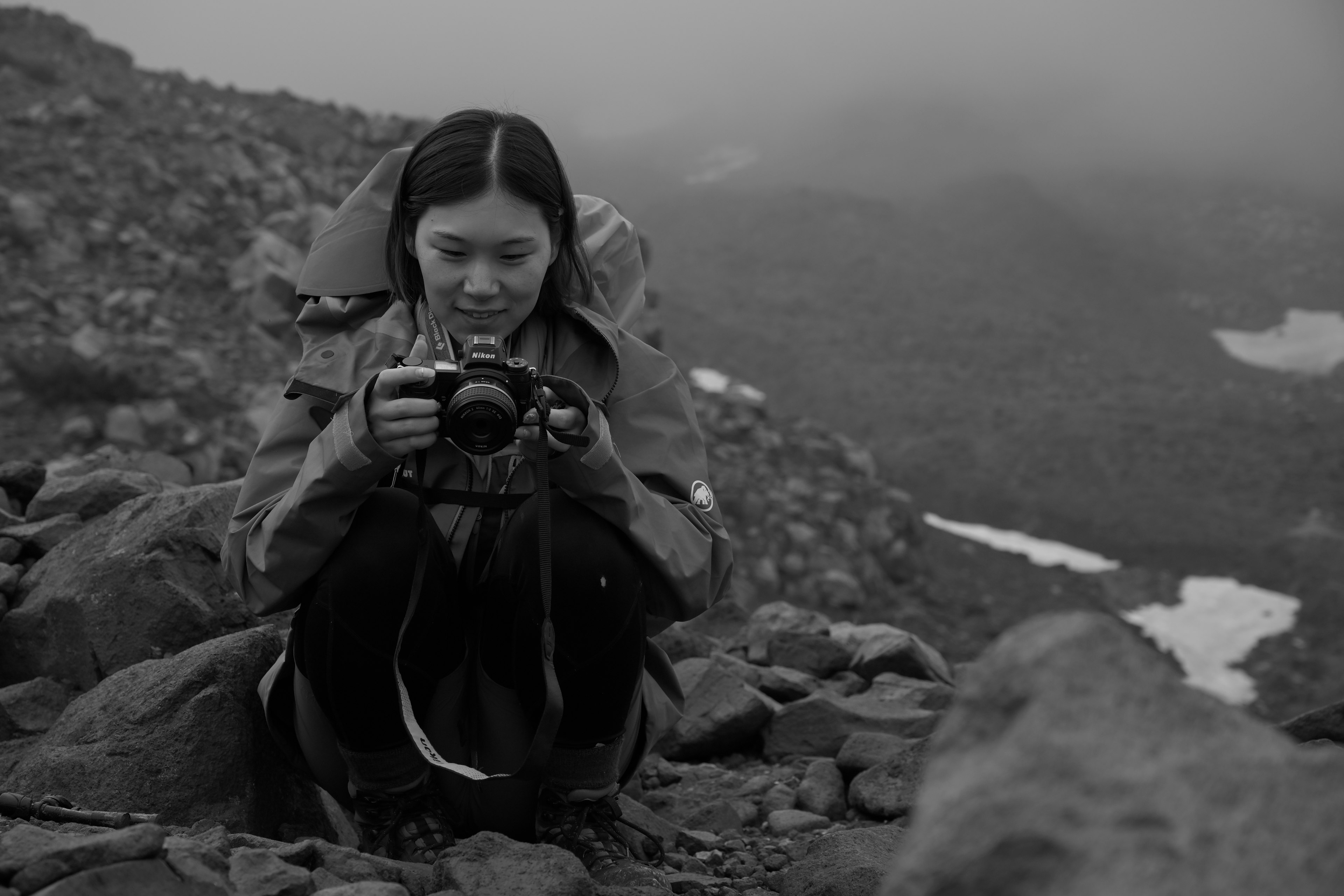 Black and white photo of a woman holding a camera on rocky terrain