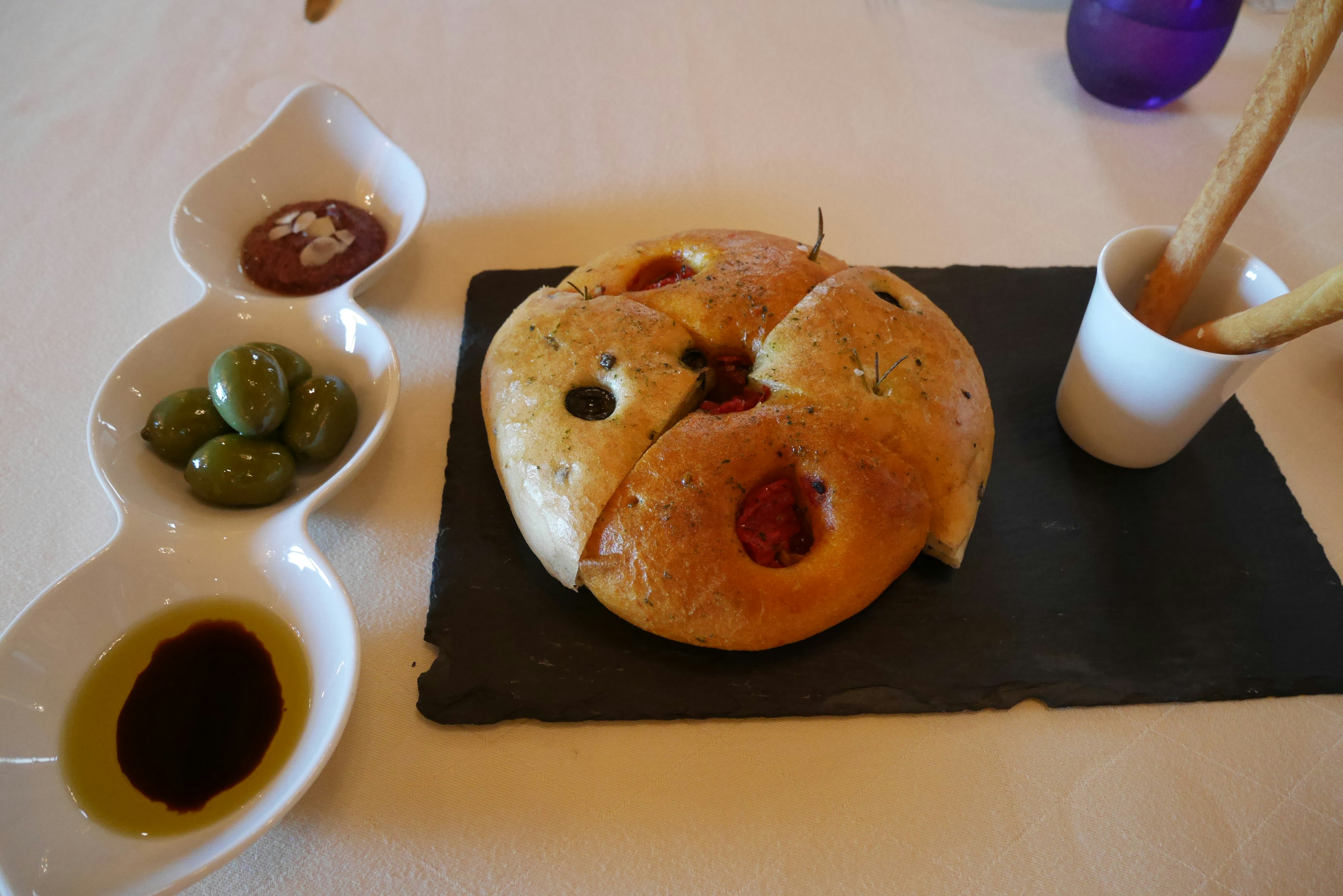 Ein runder Brot mit Oliven und Dipsaucen auf einem Schieferplatte präsentiert