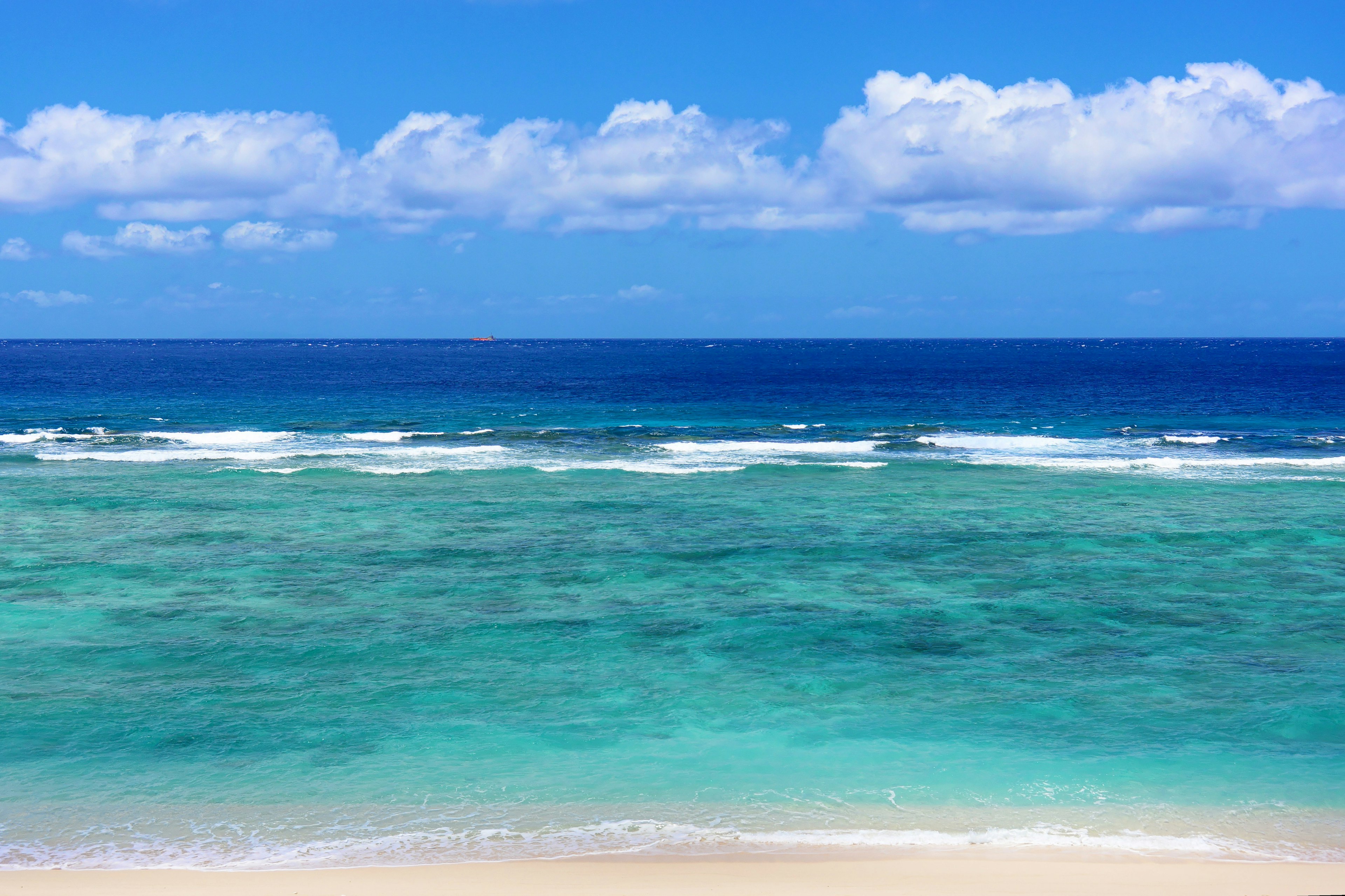 A scenic view of a blue ocean with white waves and a sandy beach