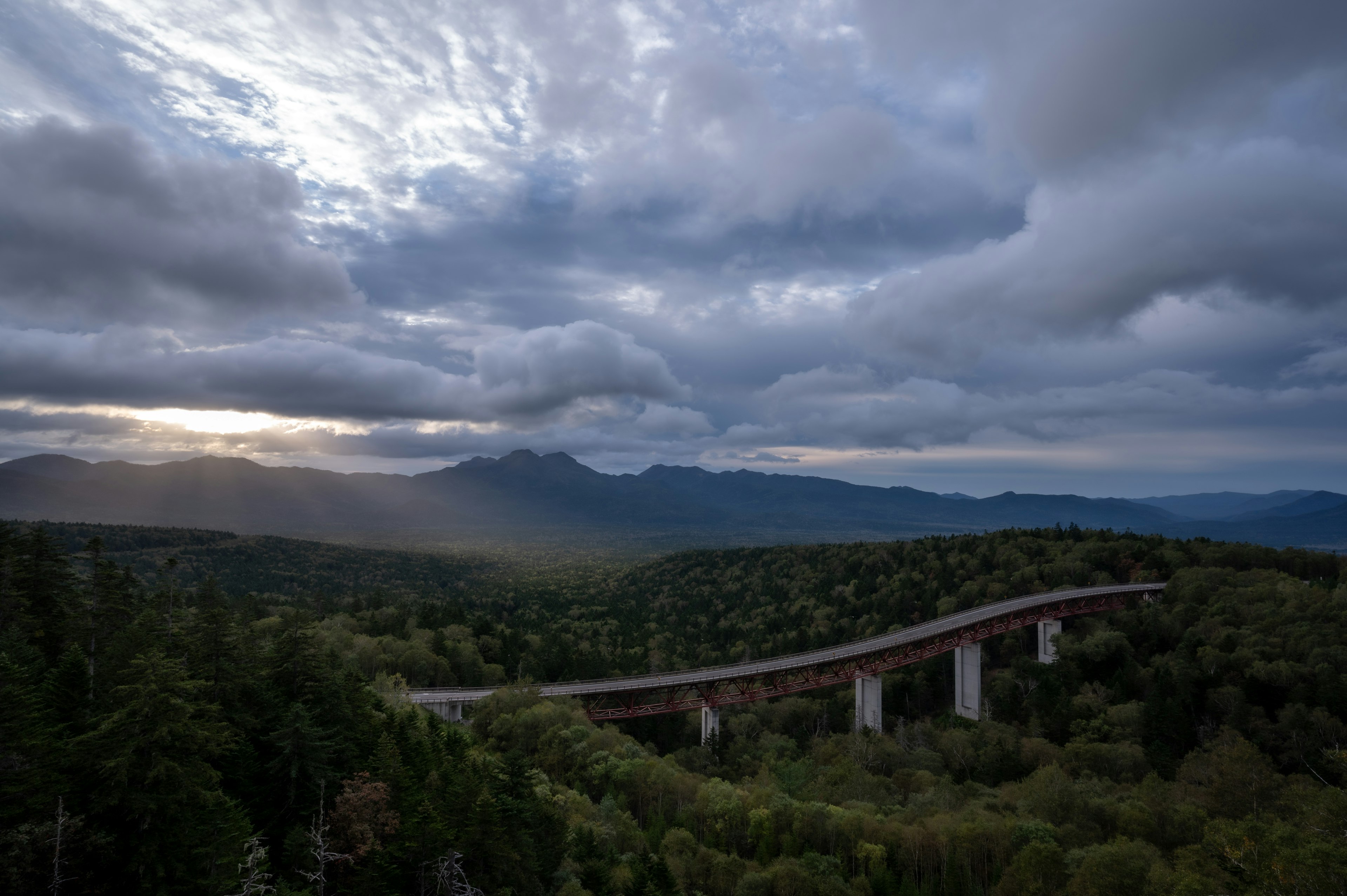 Montañas exuberantes con un puente bajo un cielo nublado y rayos de luz