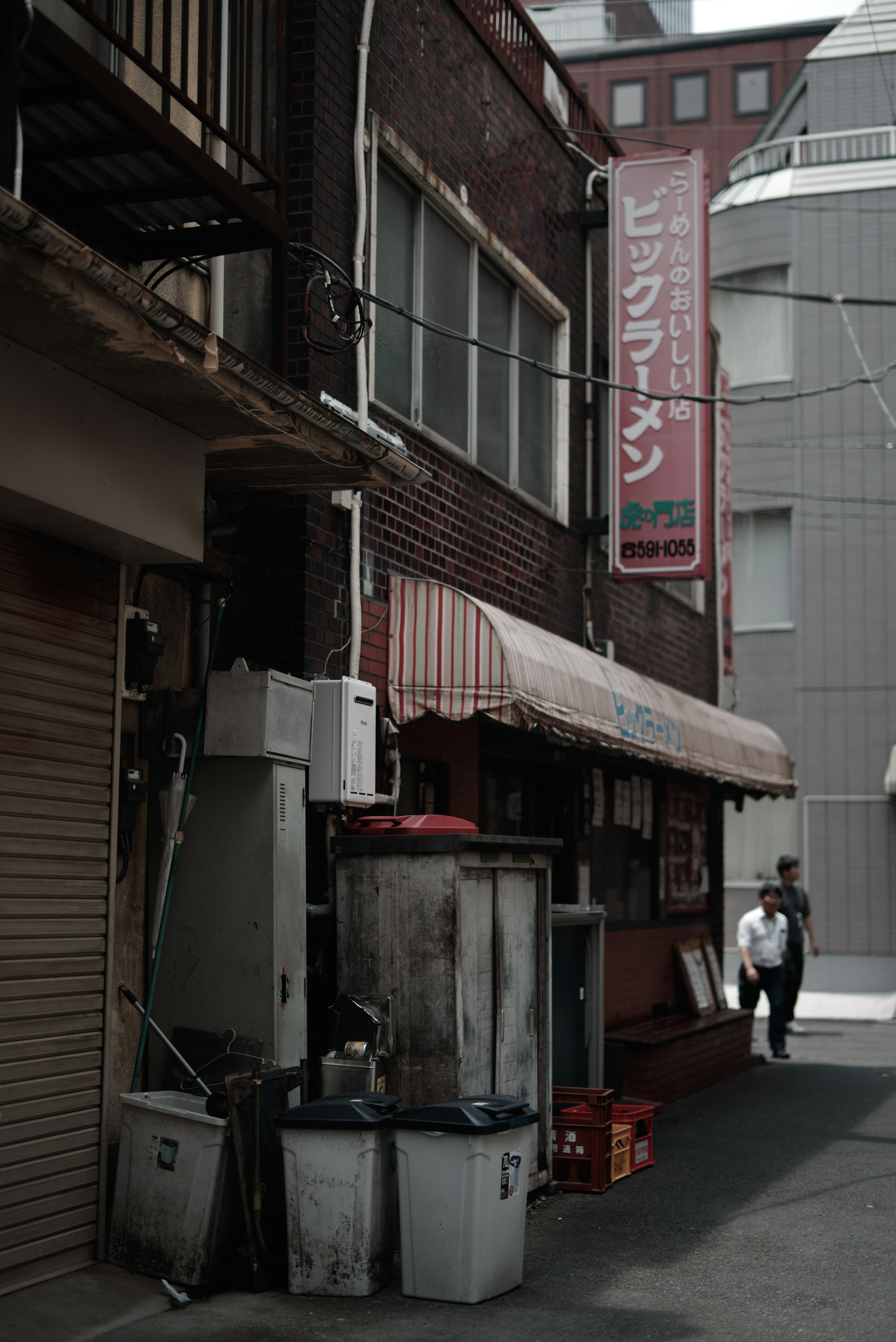 Callejón estrecho con restaurantes y botes de basura frente a edificios antiguos