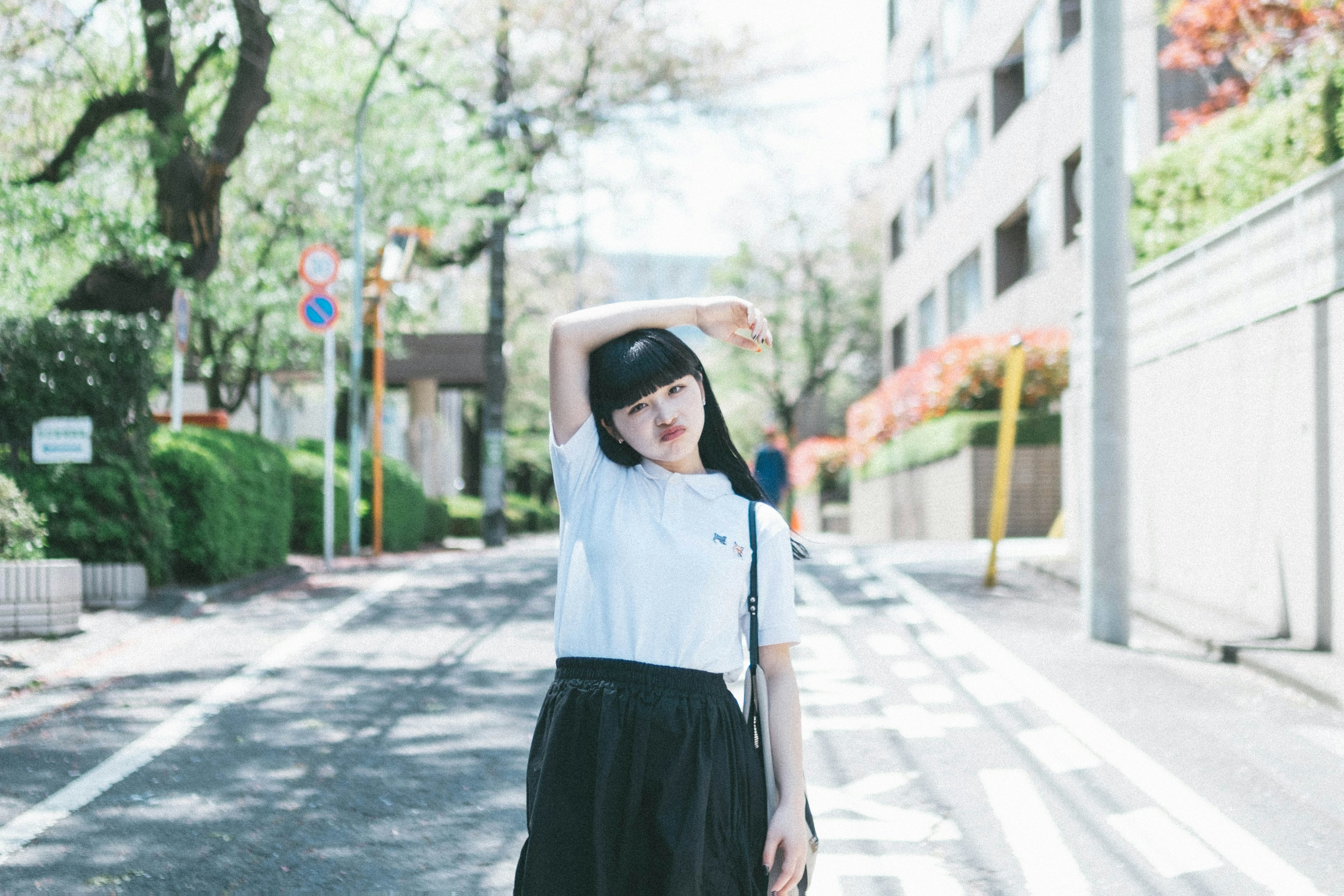 Woman posing on the street wearing a white shirt and black skirt surrounded by trees and buildings