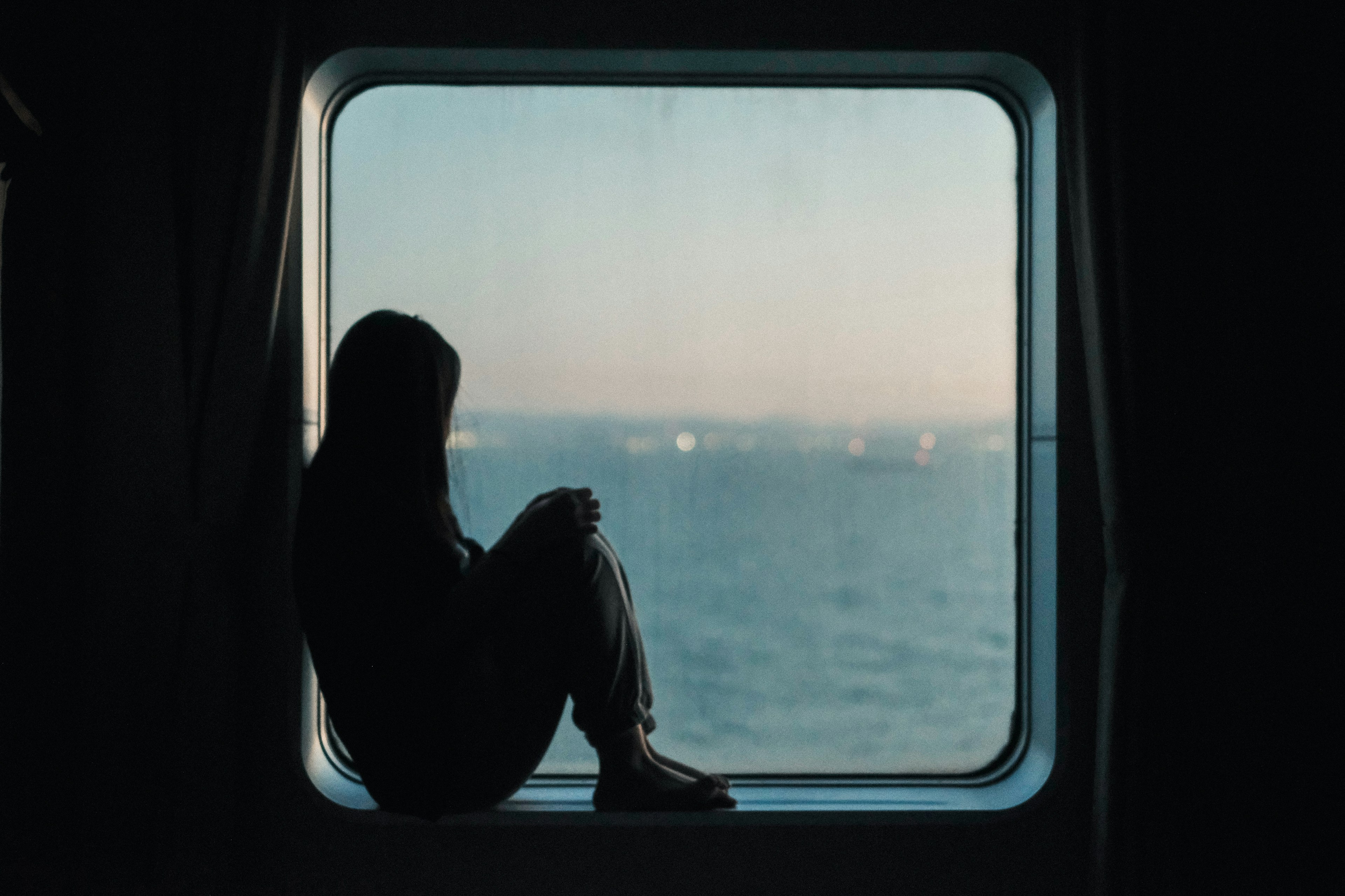 Silhouette einer Frau, die an einem Fenster mit Blick auf das Meer sitzt