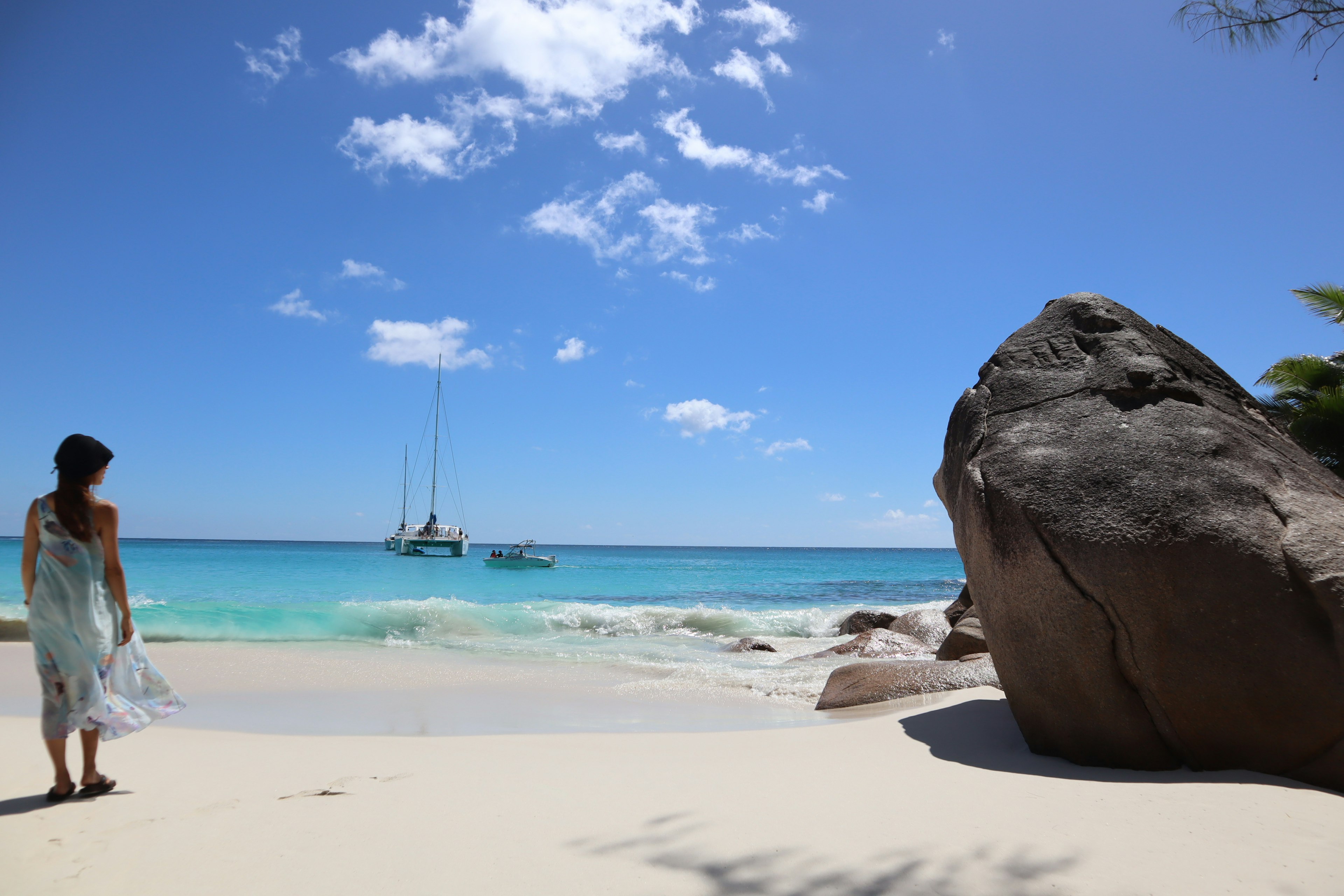 Frau, die das ruhige Meer an einem Strand mit einem großen Felsen betrachtet