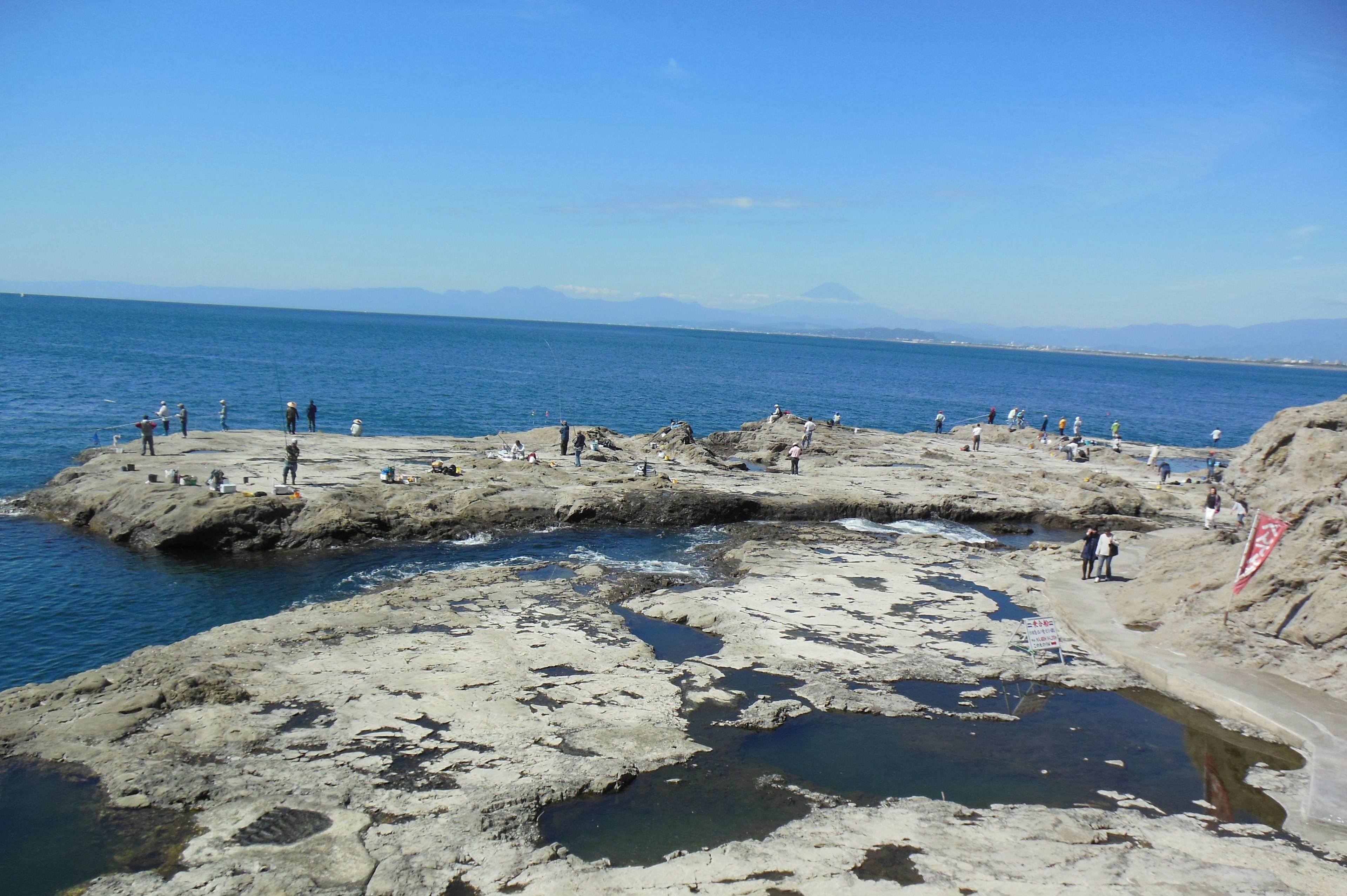 海岸の岩場に人々が集まる風景 青い海と空が広がる