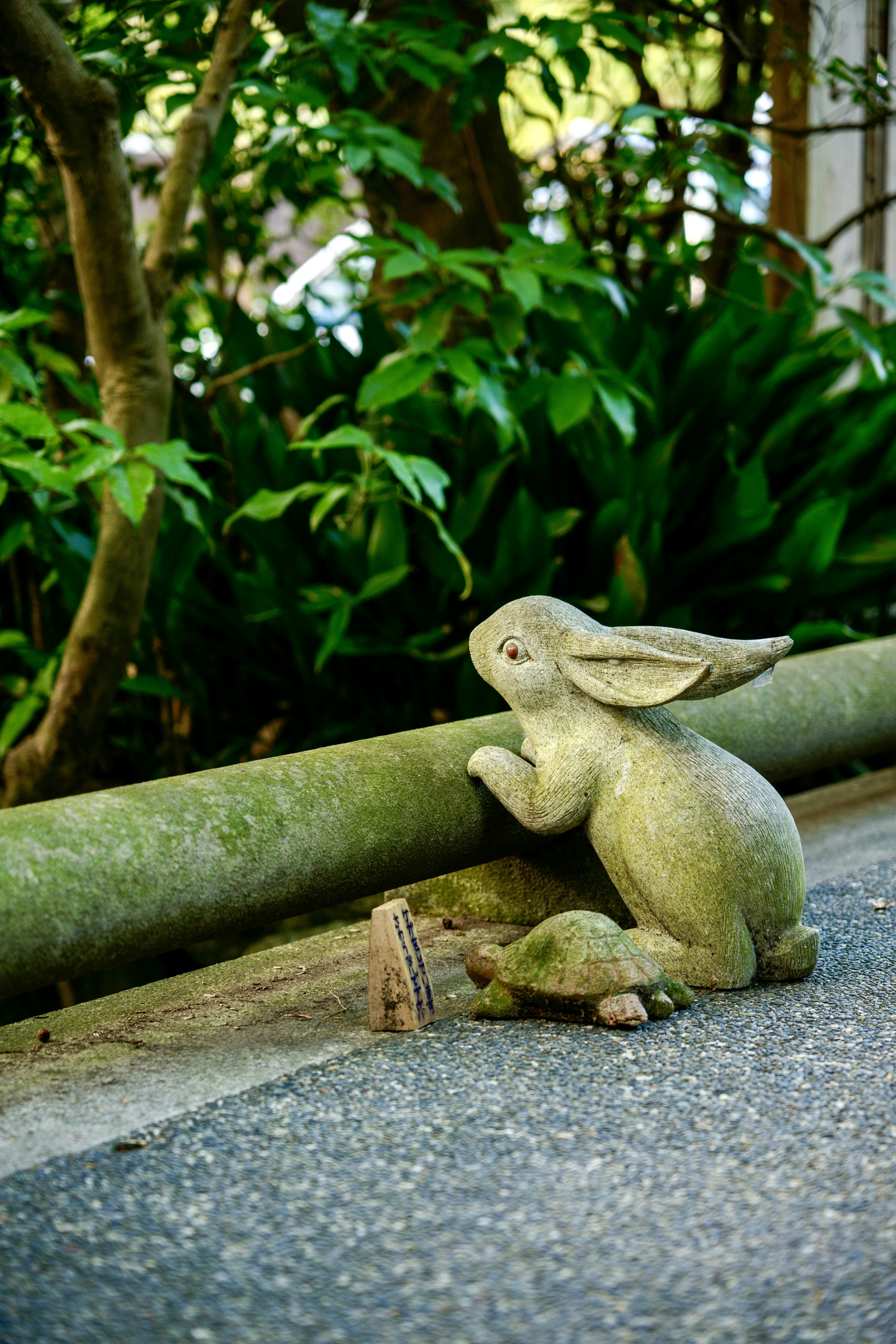 A rabbit sculpture sitting near green plants in a garden