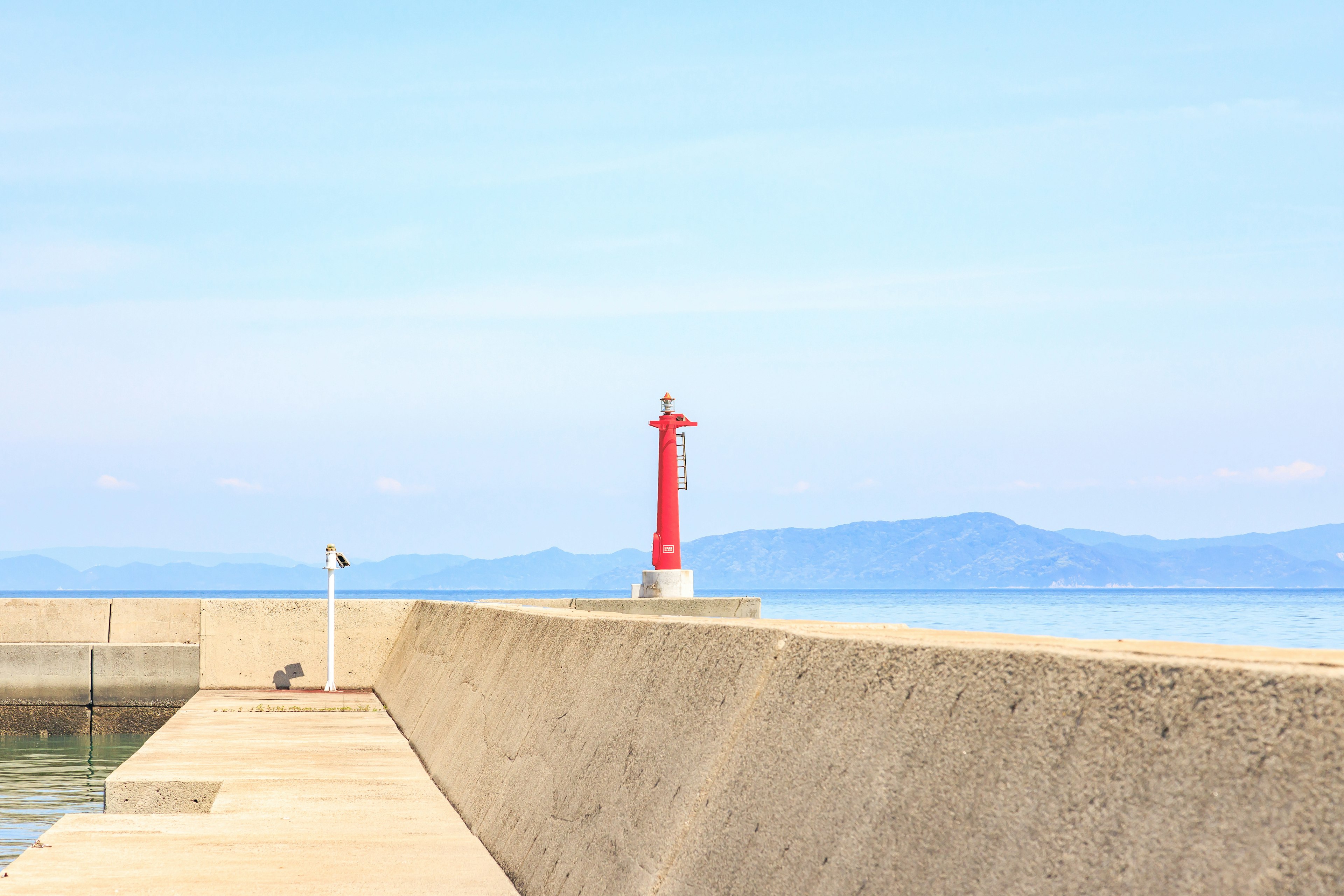 赤い灯台が海に向かって立っている防波堤の風景