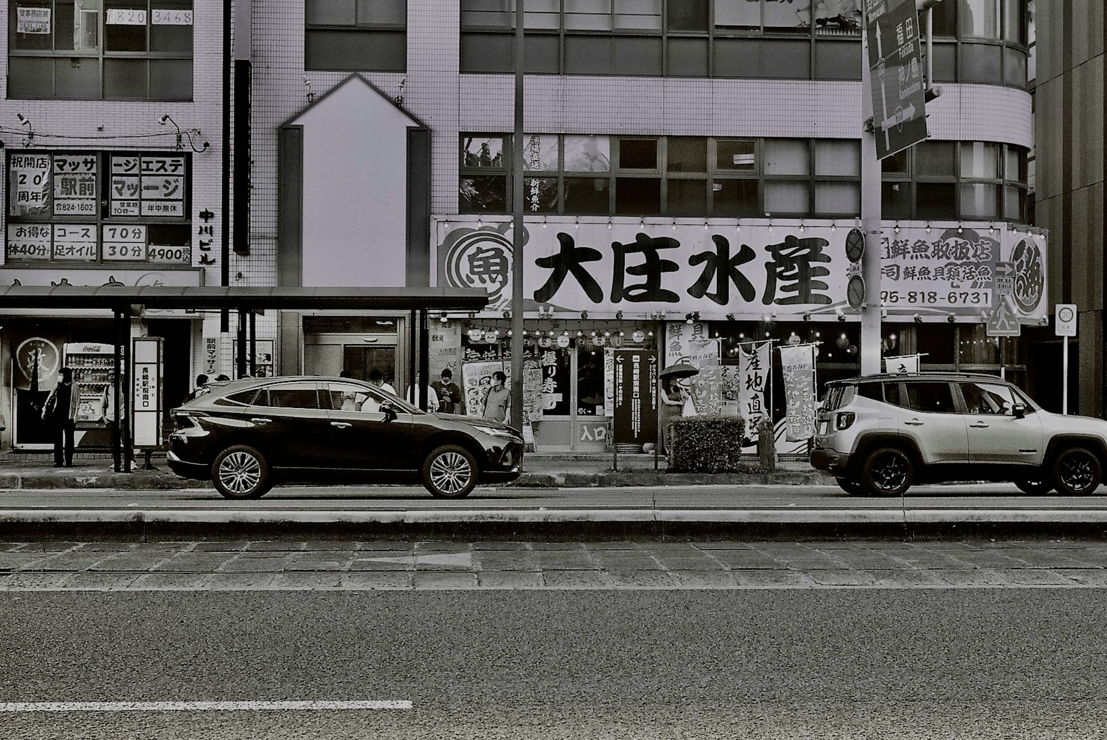 大庄水産の看板が目立つ街の風景　黒い車と白い車が並ぶ