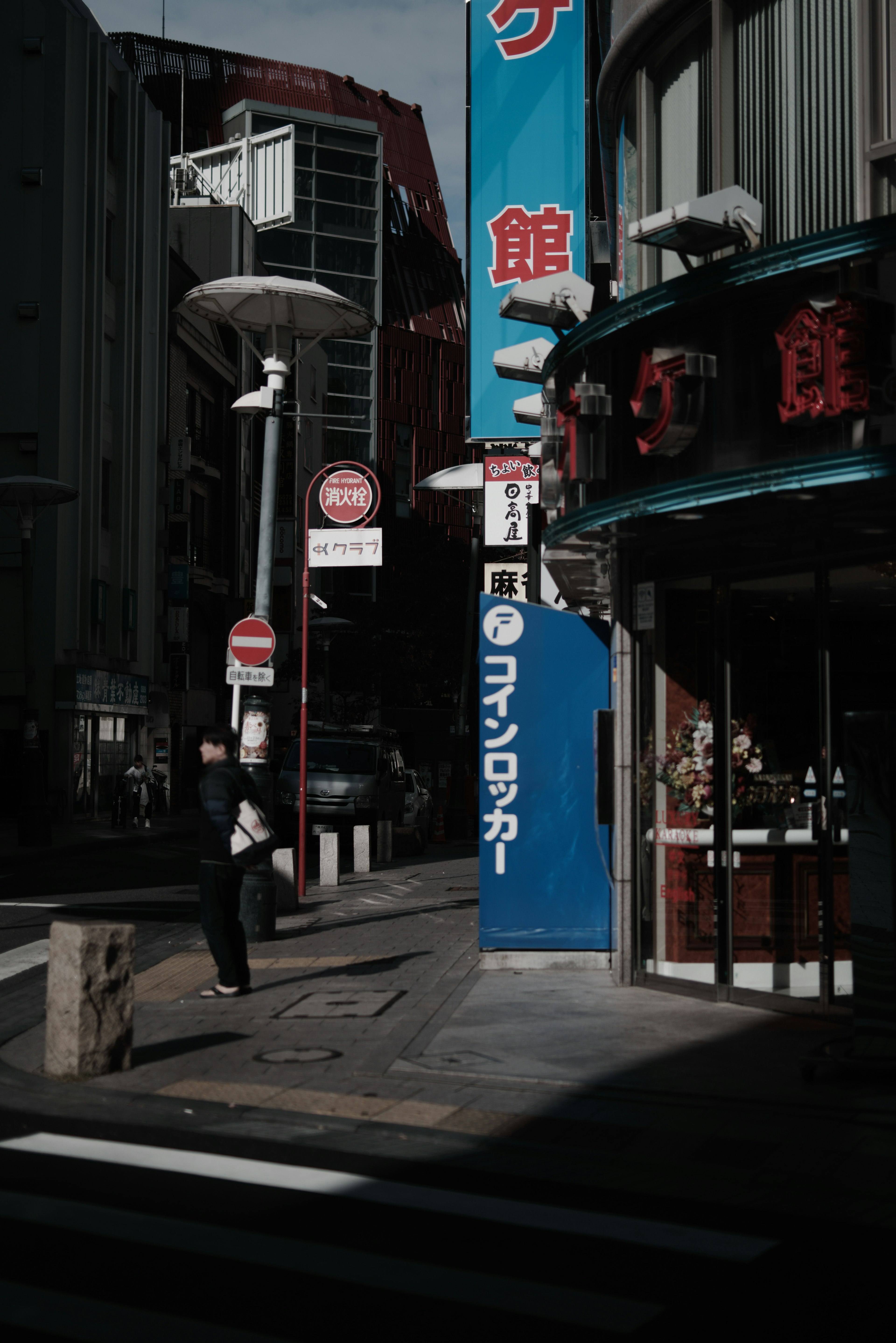 Straßenecke mit blauem Schild und Restaurantfassade im Schatten