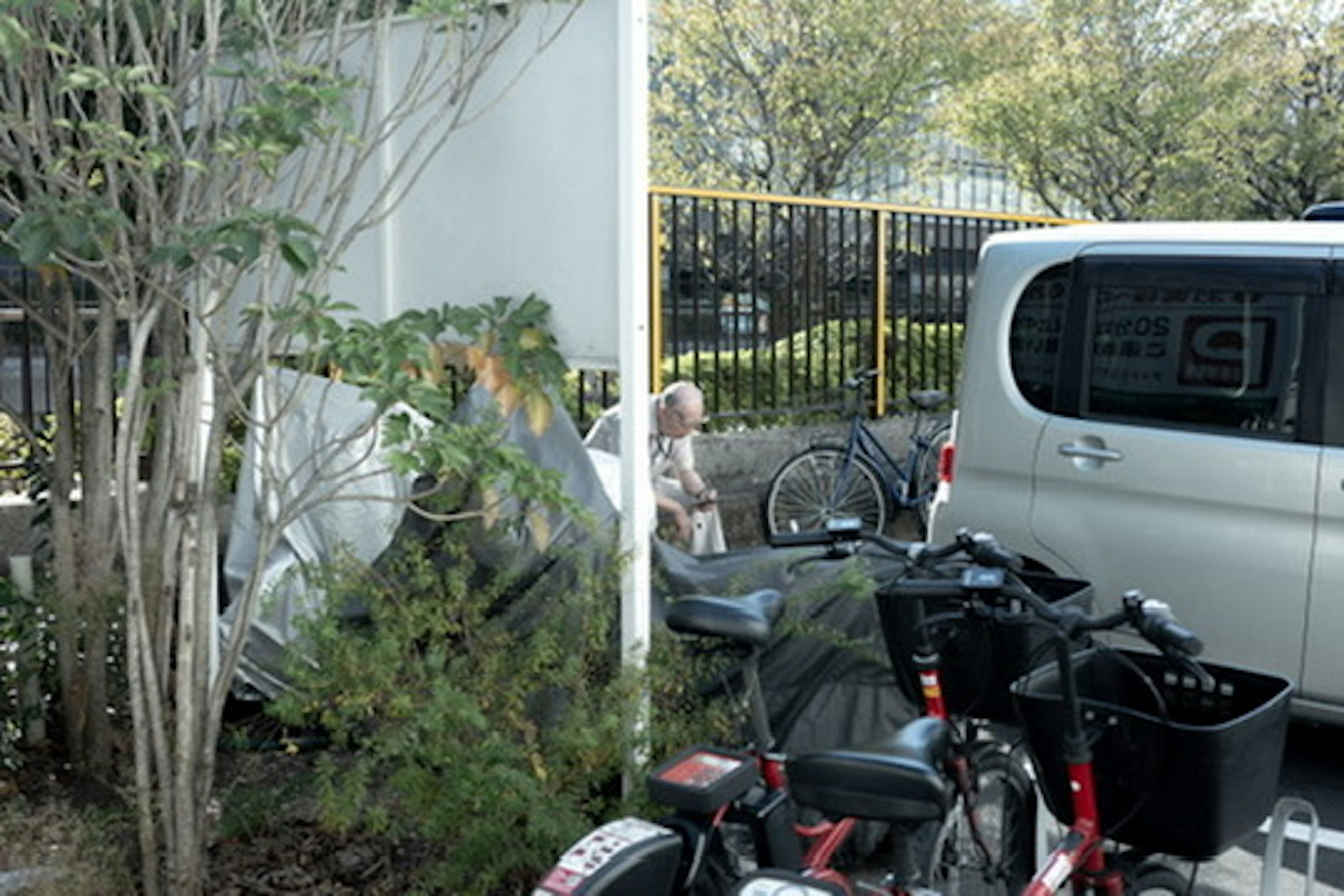 Scène avec des bicyclettes et une voiture garée entourée de verdure et une personne en arrière-plan