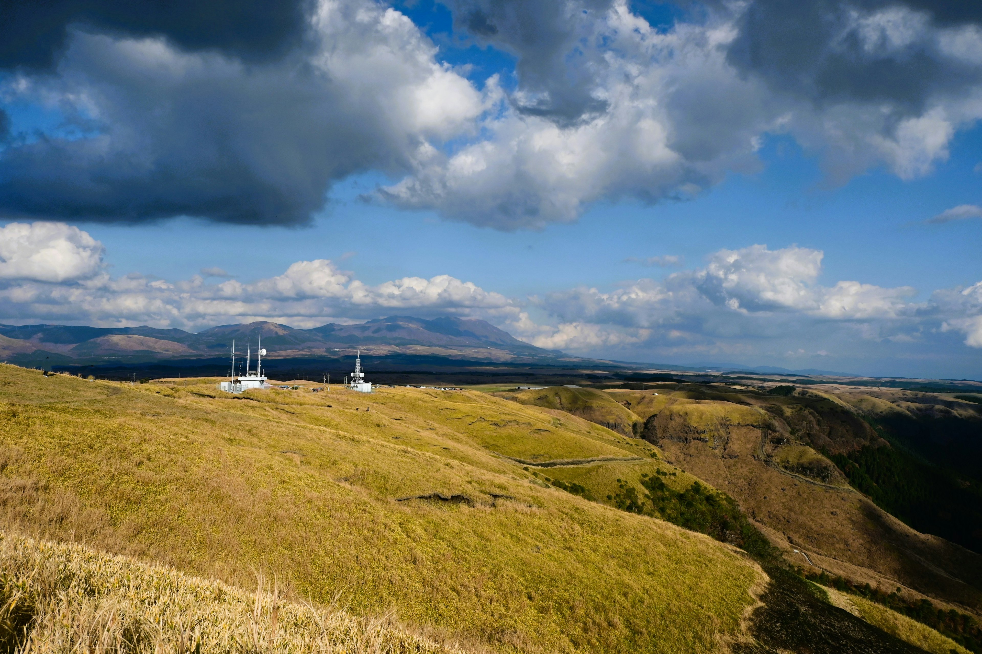 Landscape of communication towers on a grassy hill under a blue sky and clouds