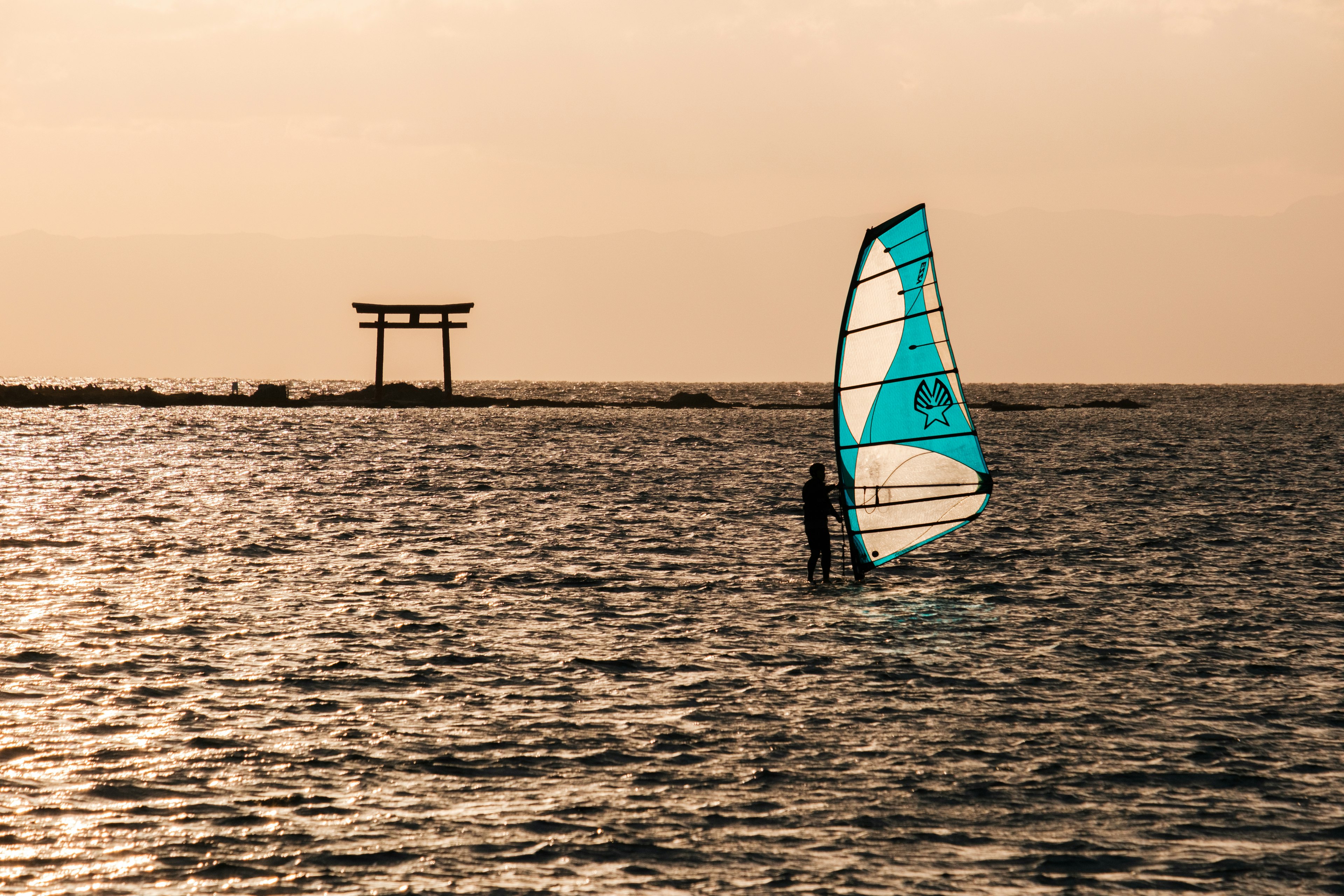 Personne faisant du windsurf sur la mer avec une silhouette de torii en arrière-plan