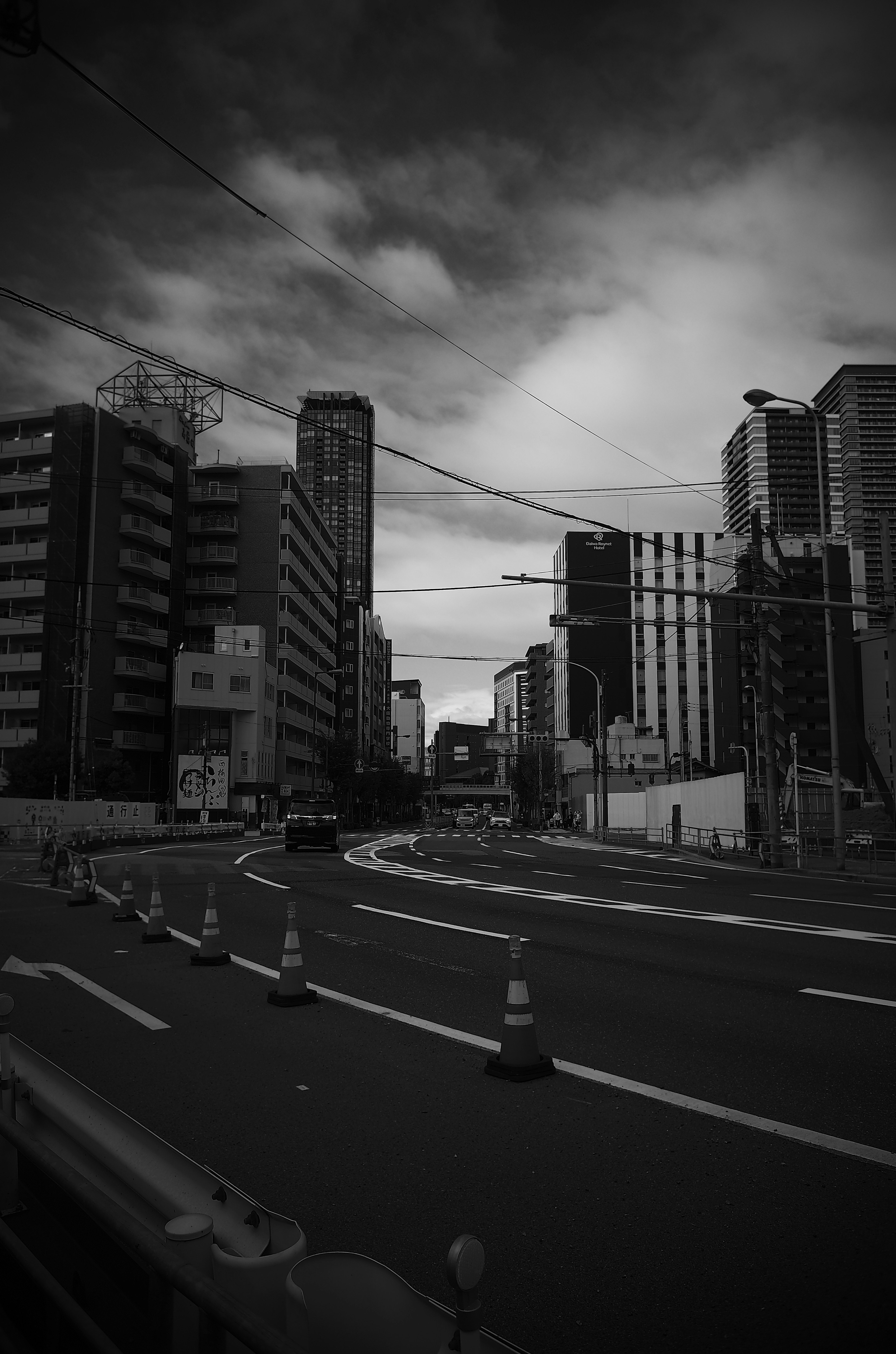 Black and white urban landscape with traffic cones on the road and tall buildings in the background