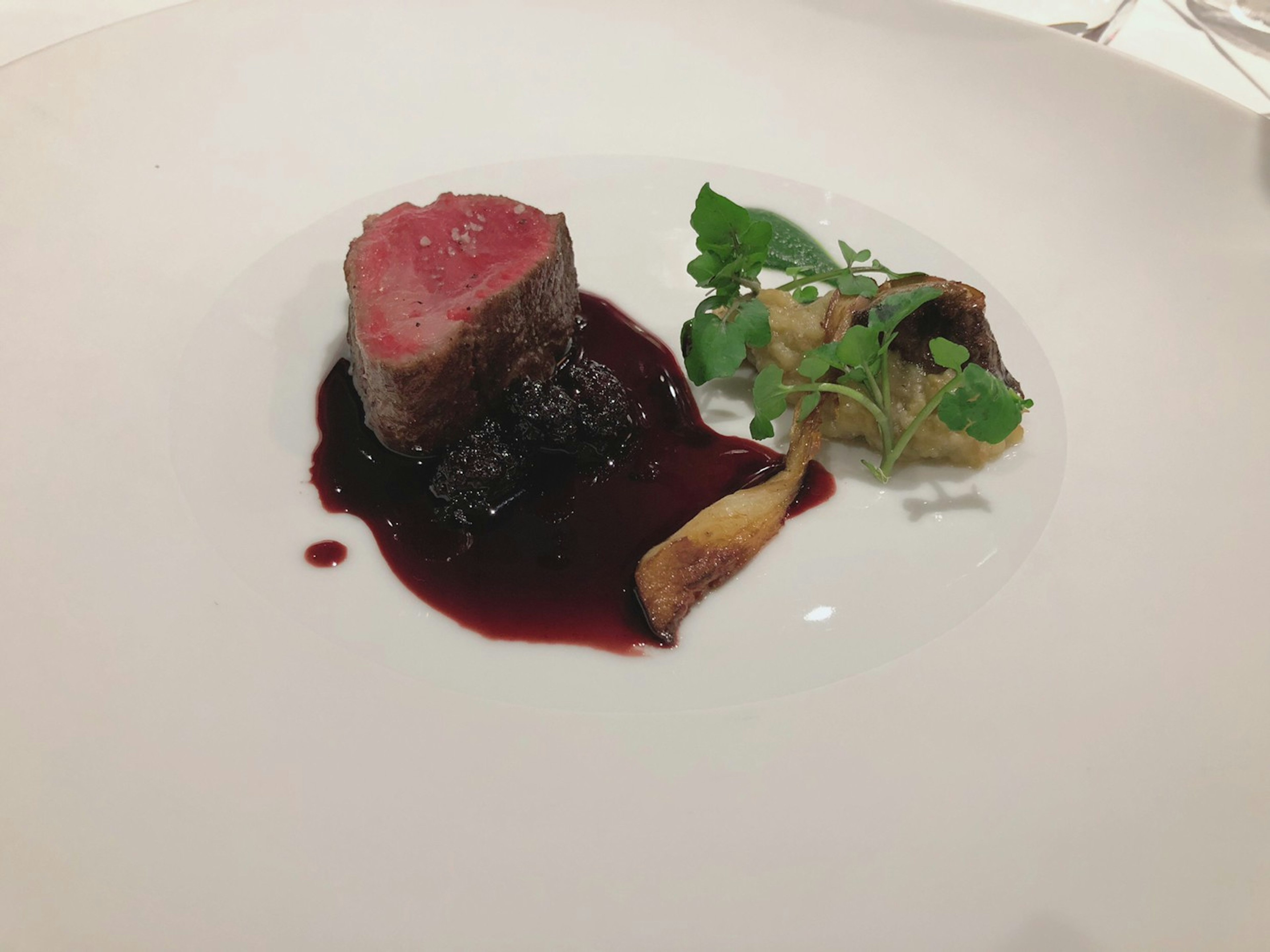 Plate featuring sliced red meat with berry sauce and garnished with greens