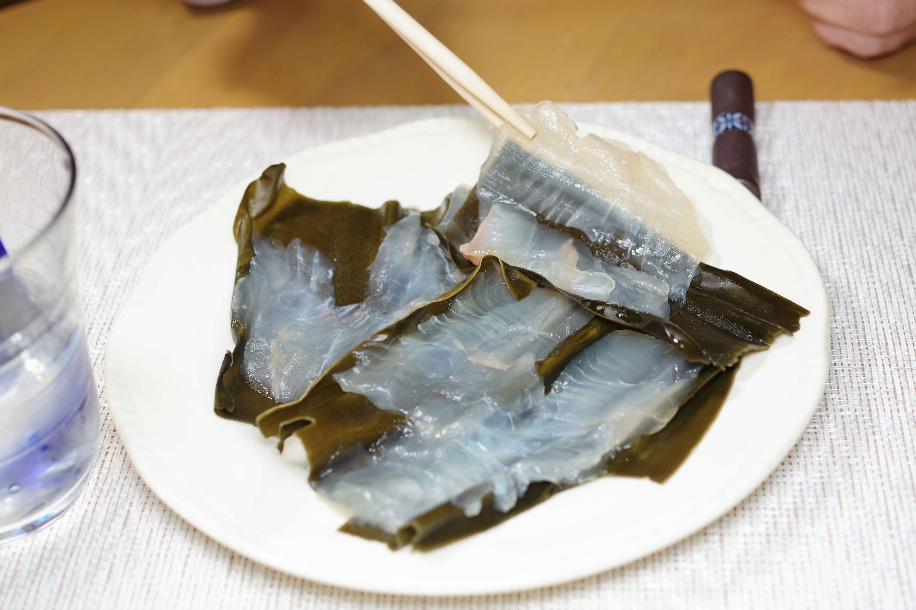 Transparent seaweed on a plate with a piece being held by chopsticks