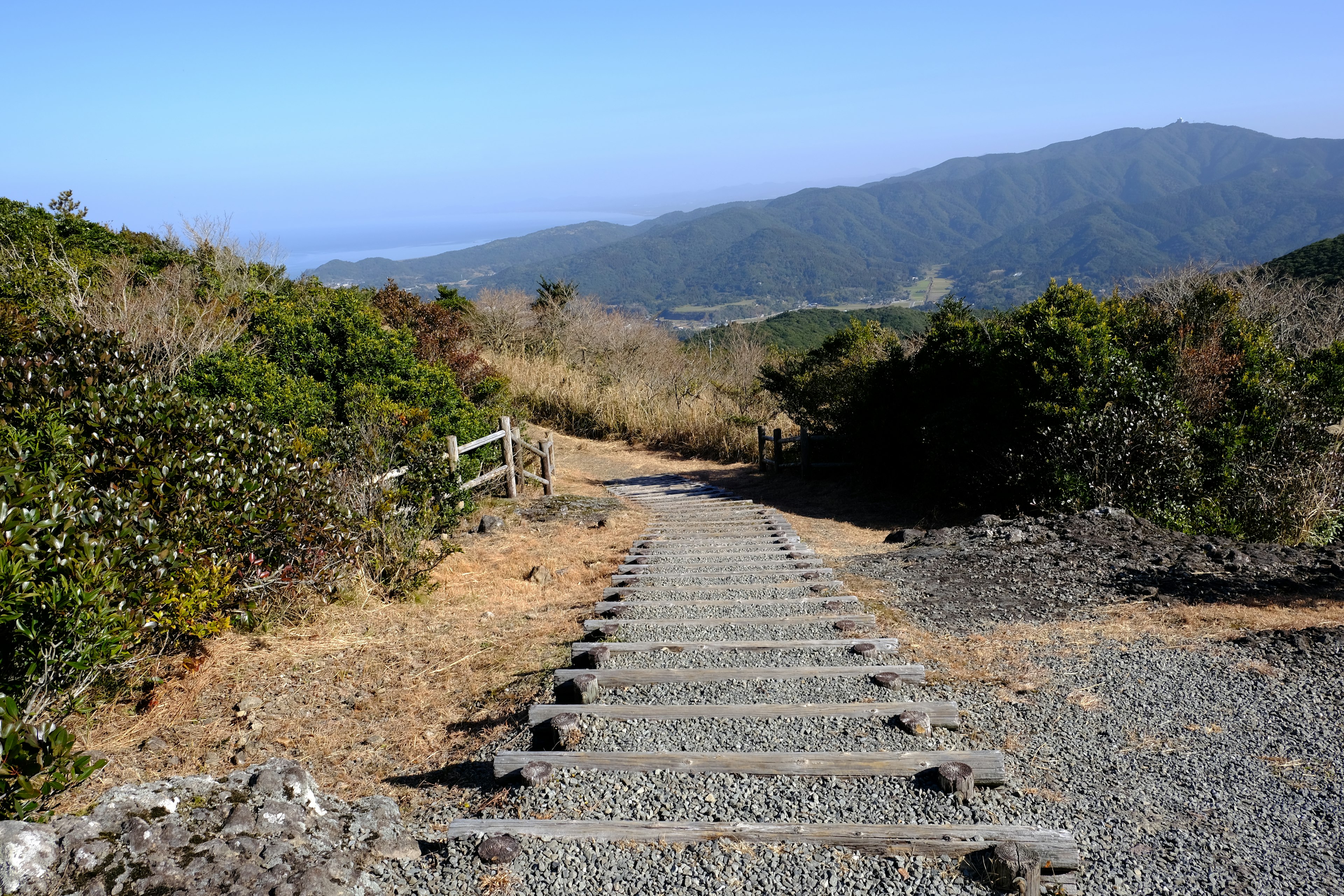 Escaleras de piedra que descienden por un sendero de montaña con vegetación y montañas distantes