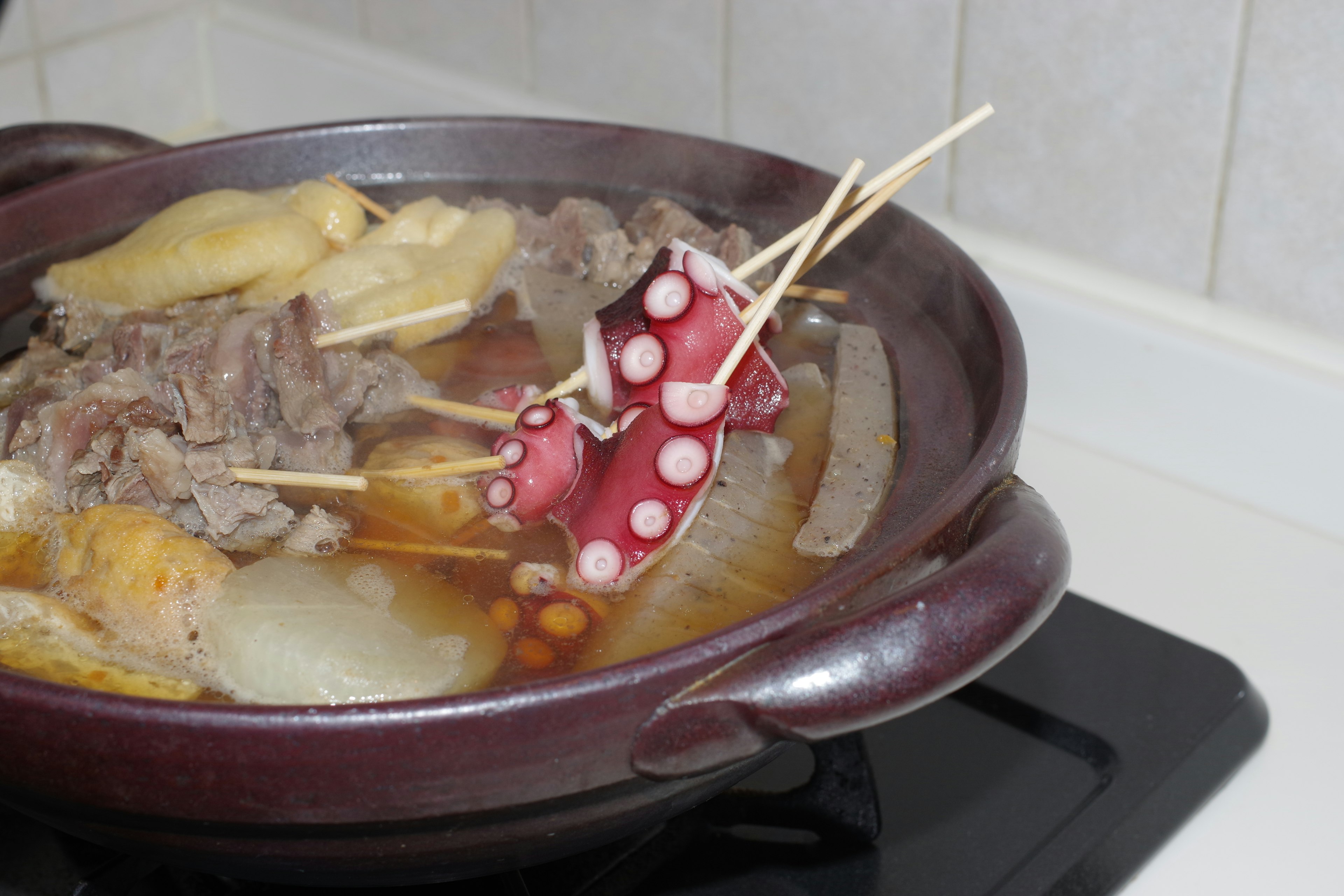 Patas de pulpo y rodajas de carne en una olla caliente