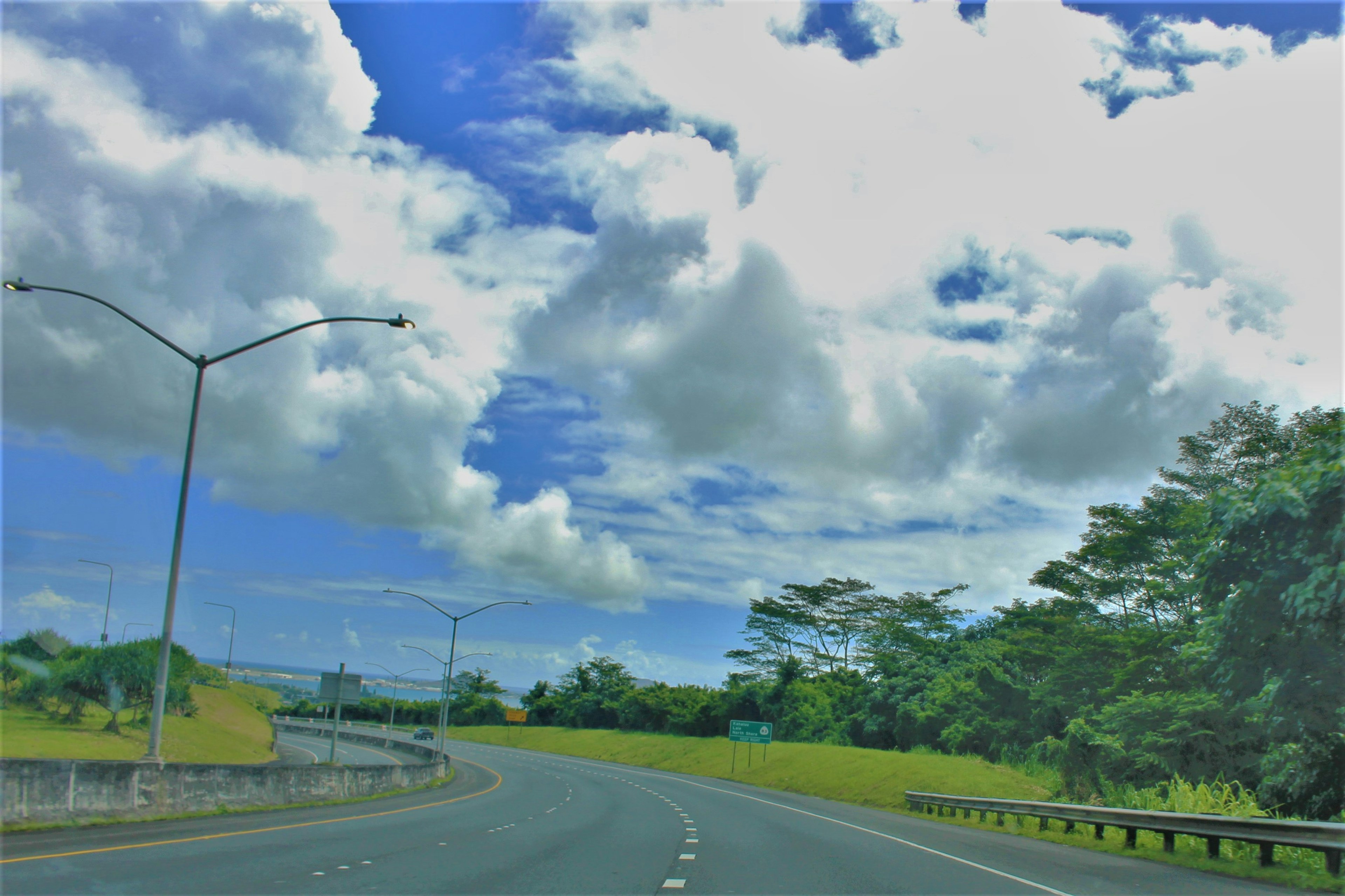 Vista escénica de una carretera bajo un cielo azul con nubes blancas árboles verdes a los lados