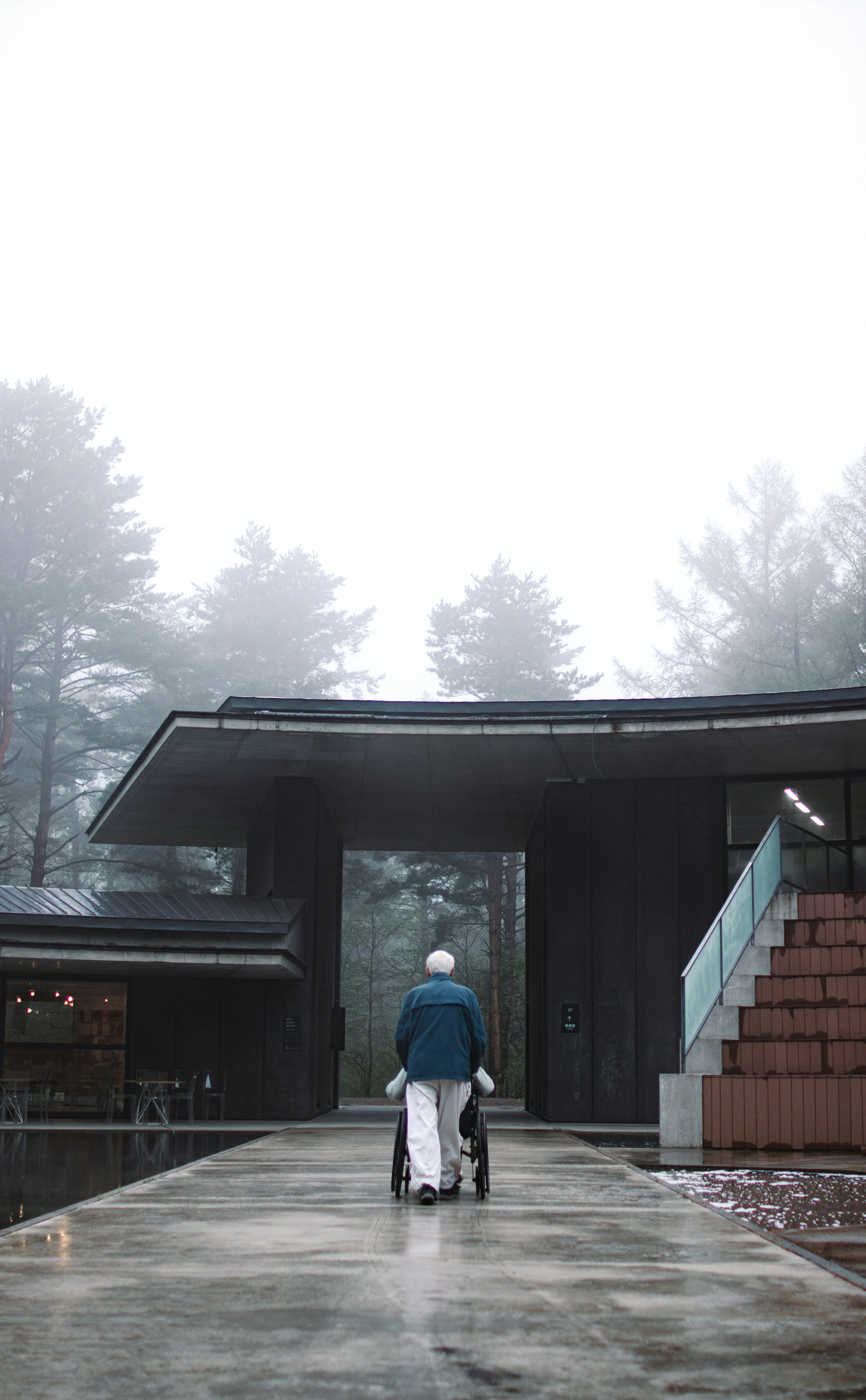 Elderly person walking in fog towards modern architecture