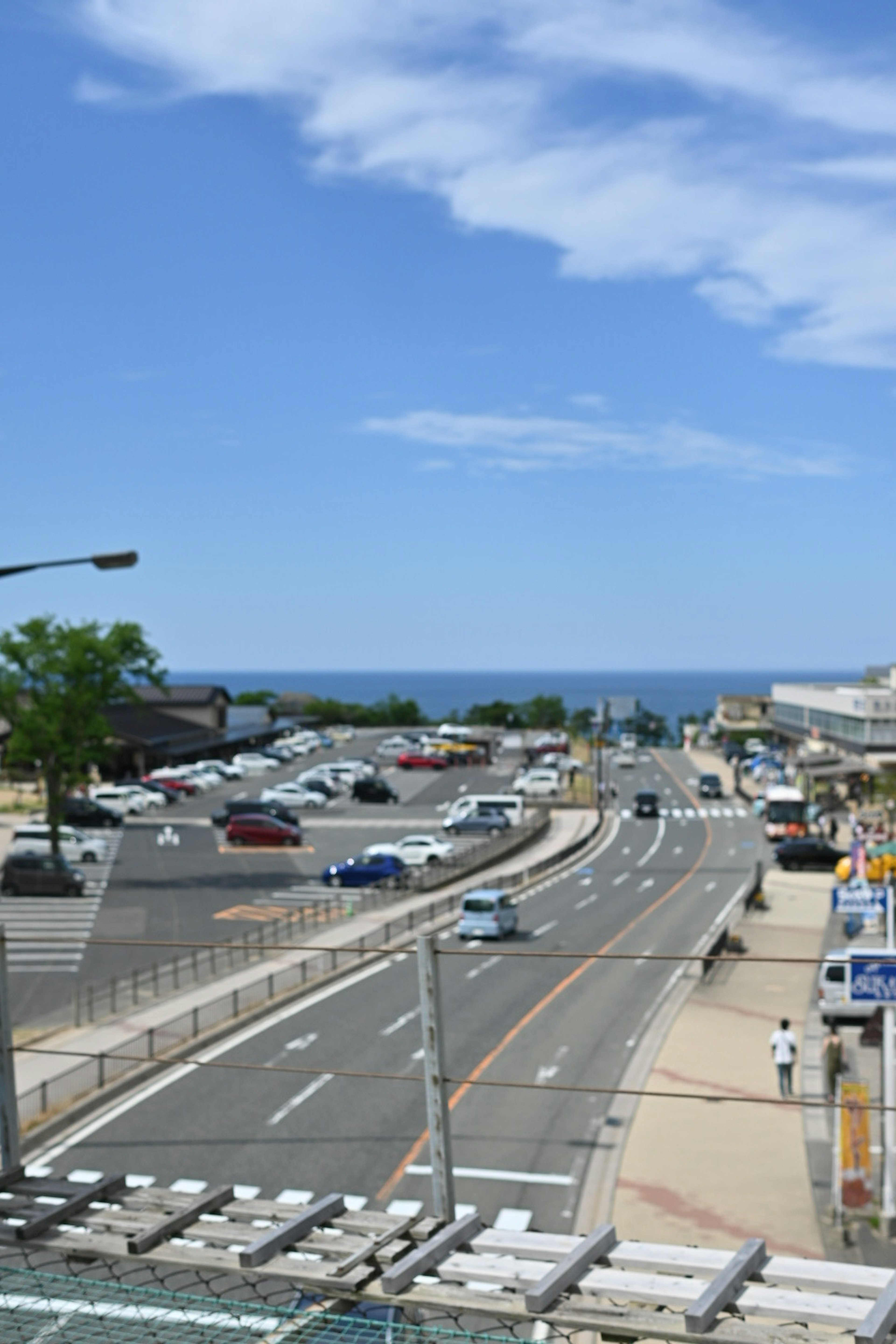 A scenic view of a road with blue sky and ocean in the background featuring cars and a parking lot