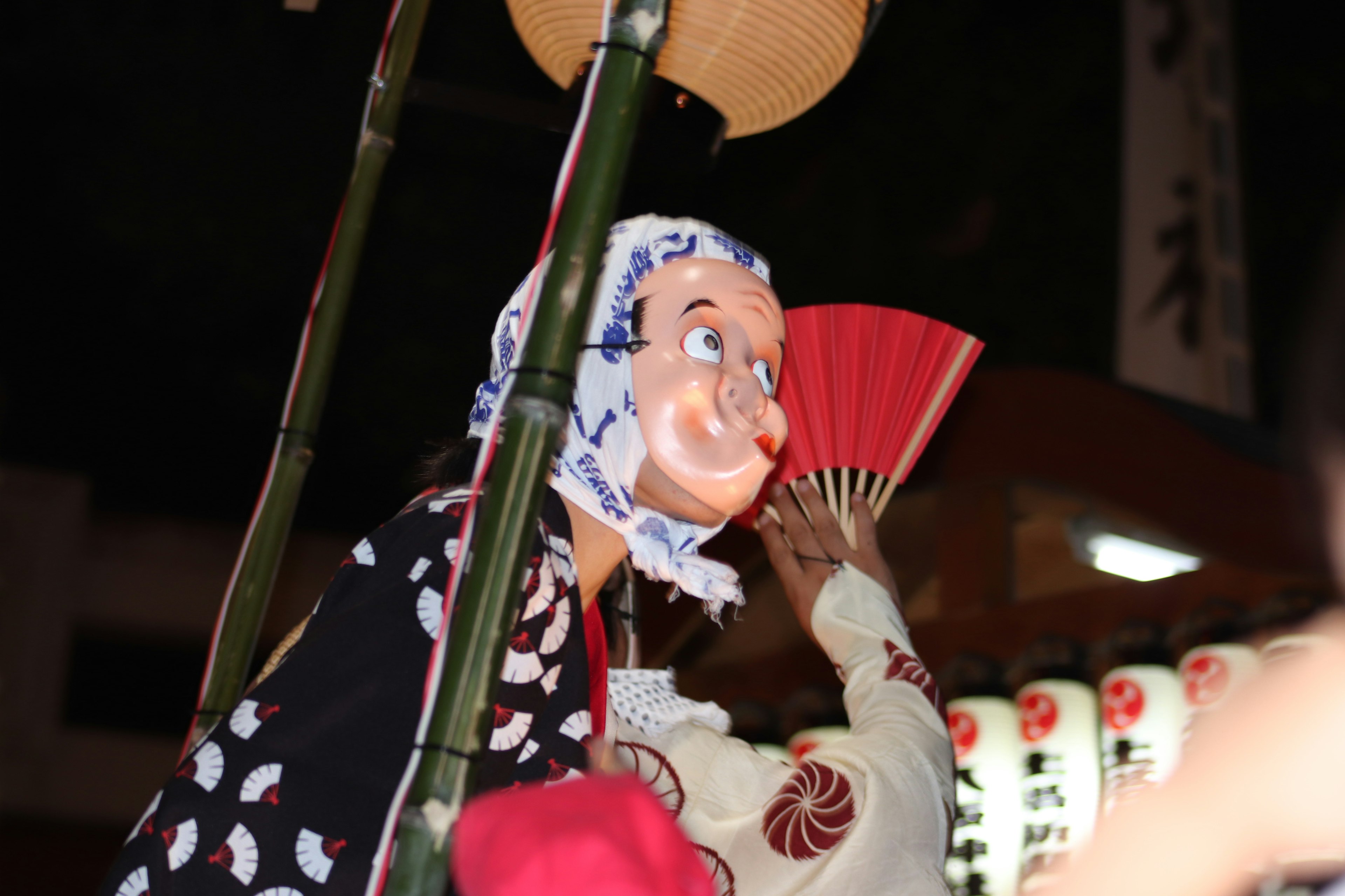 Marioneta tradicional y participante sosteniendo un abanico en un festival nocturno