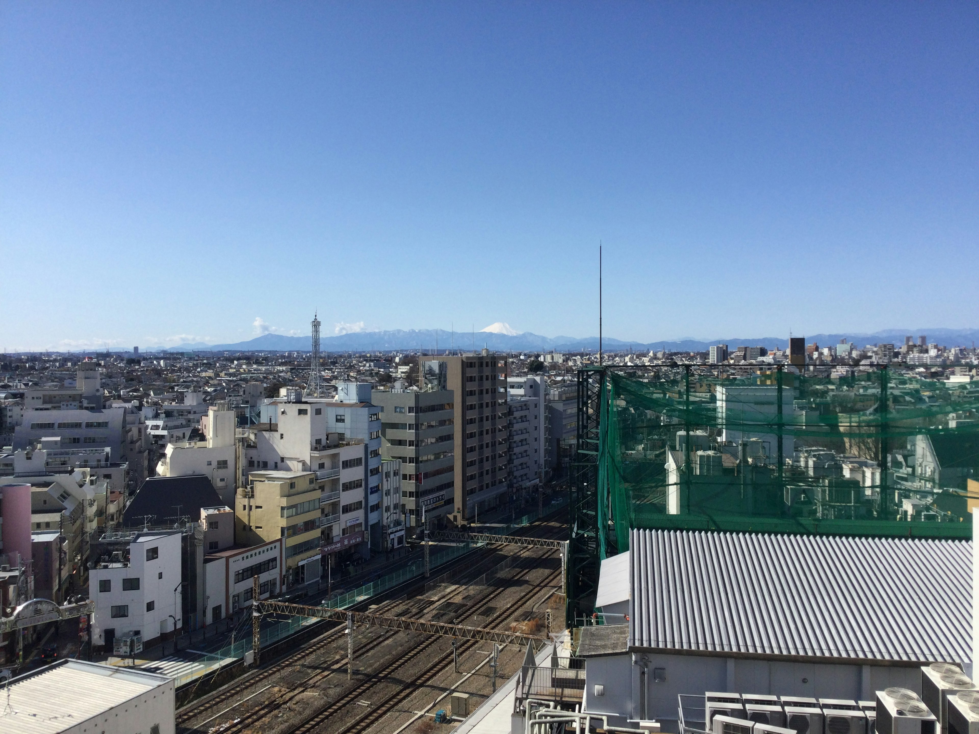 A cityscape under a clear blue sky with snow-capped mountains in the distance