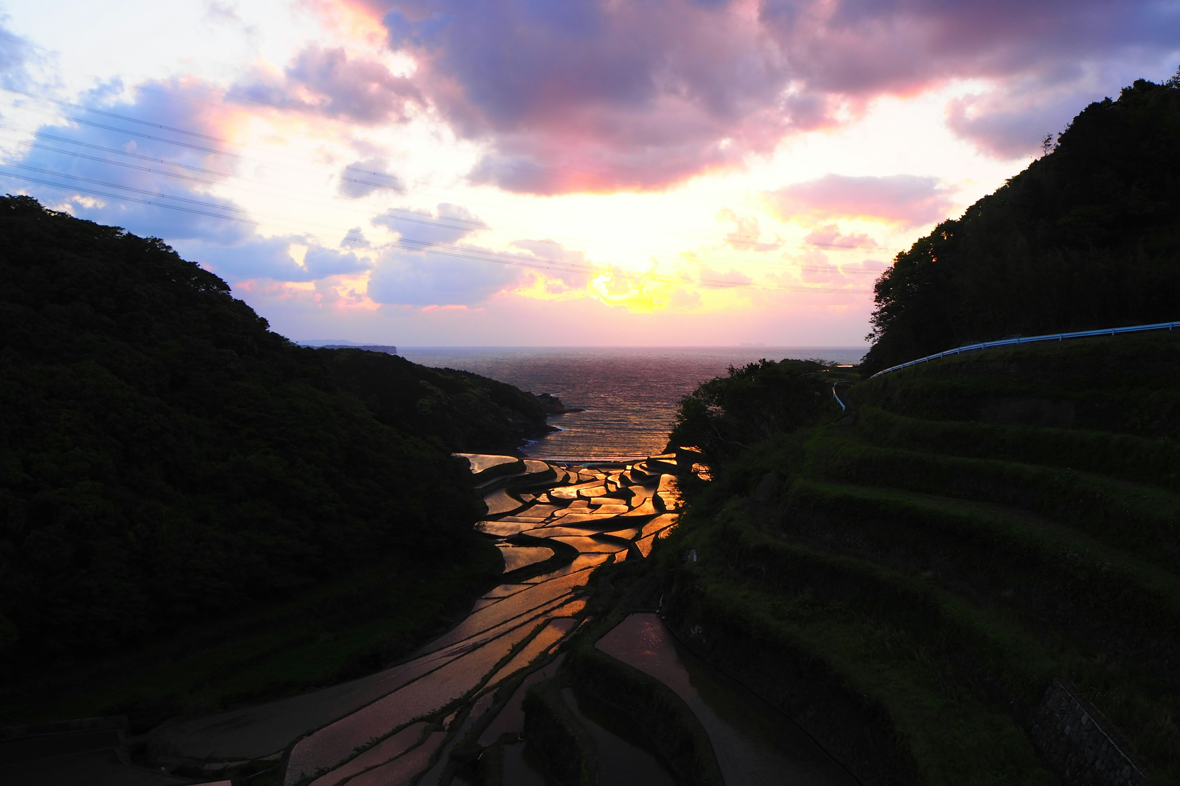 Beeindruckender Sonnenuntergang über Terrassenreisfeldern im Kontrast zum Meer und den Bergen