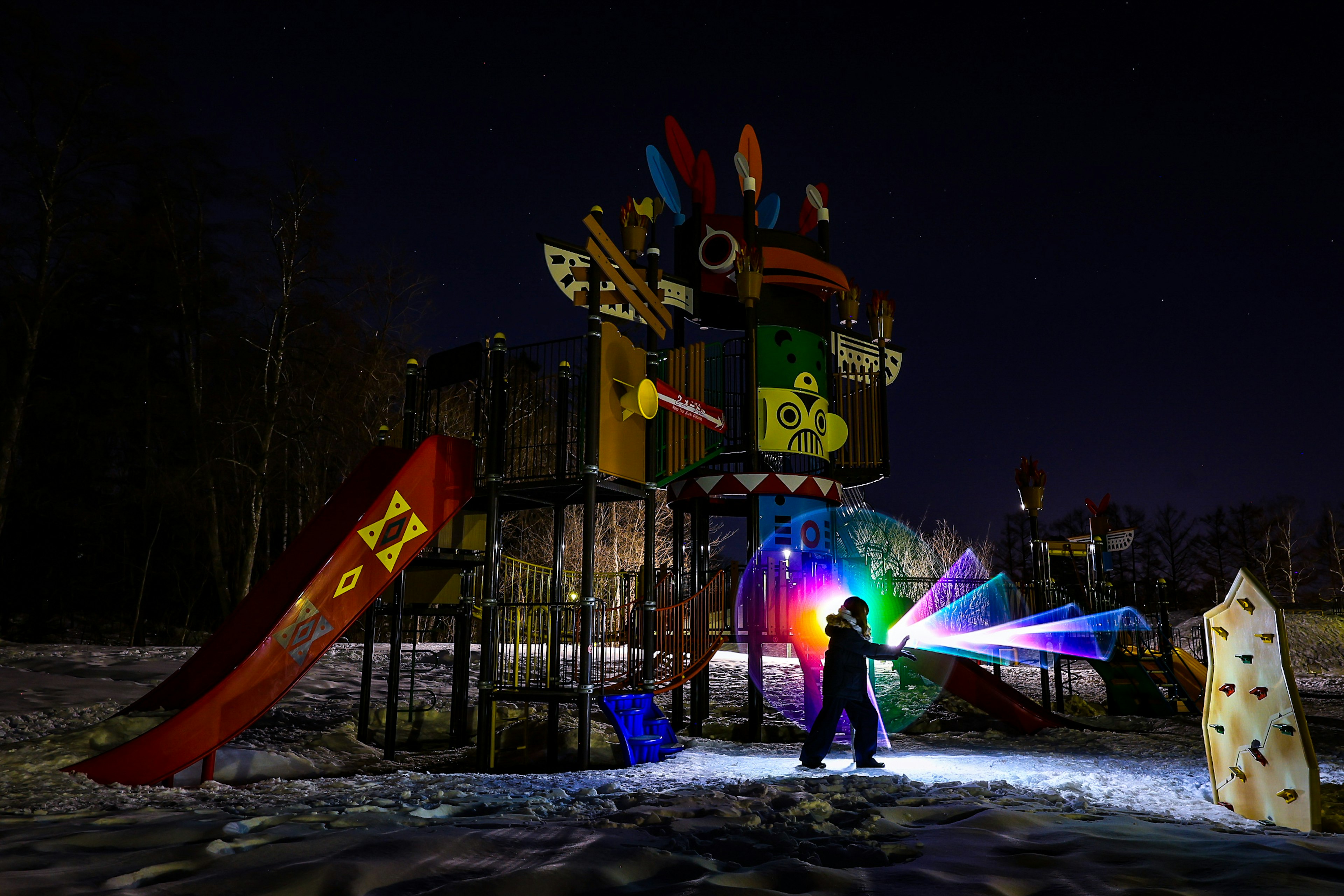 夜の公園でカラフルな遊具と雪の中で光を使って遊ぶ子供