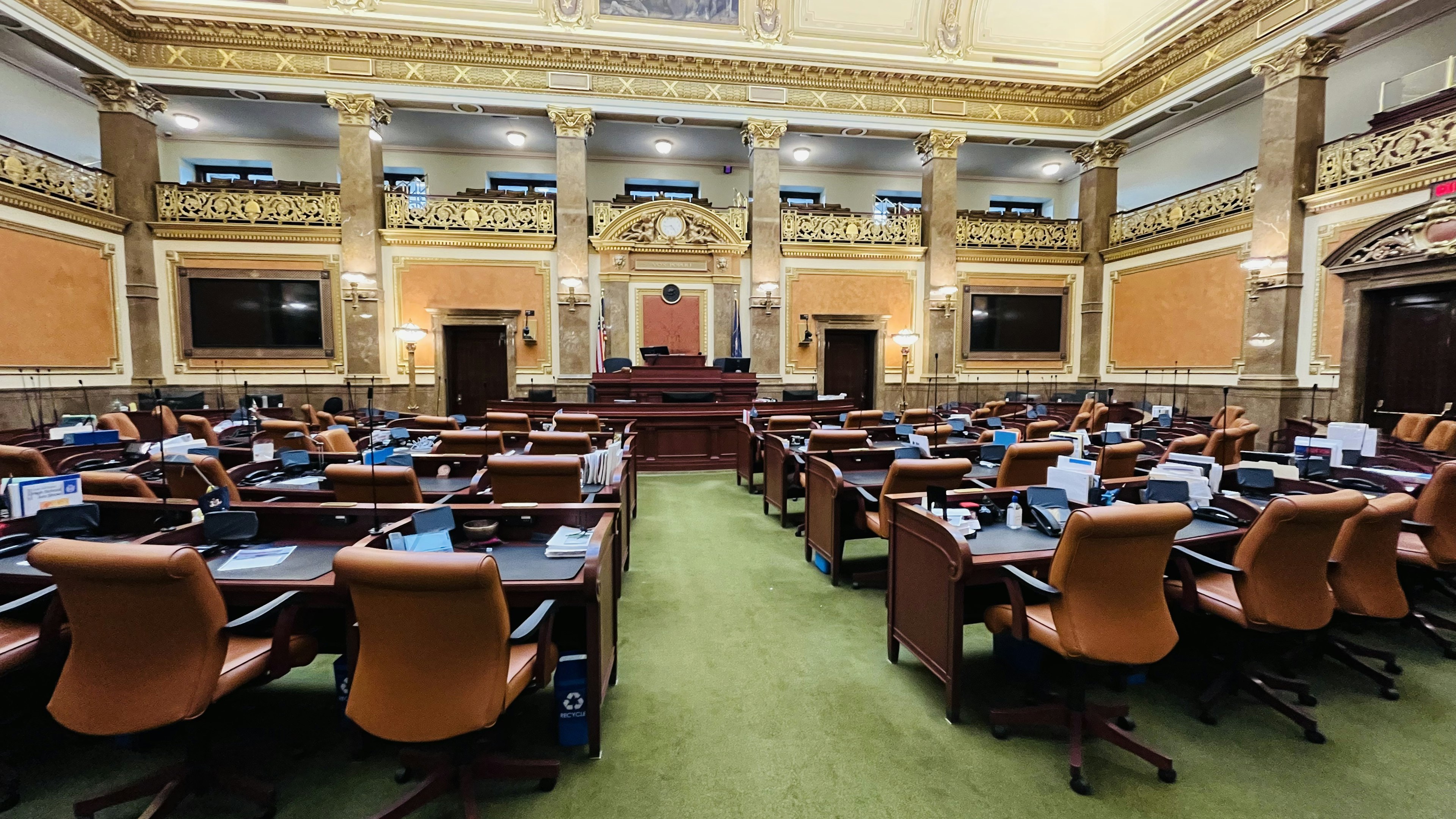 Interior of a legislative chamber with orange chairs and green carpet decorative walls